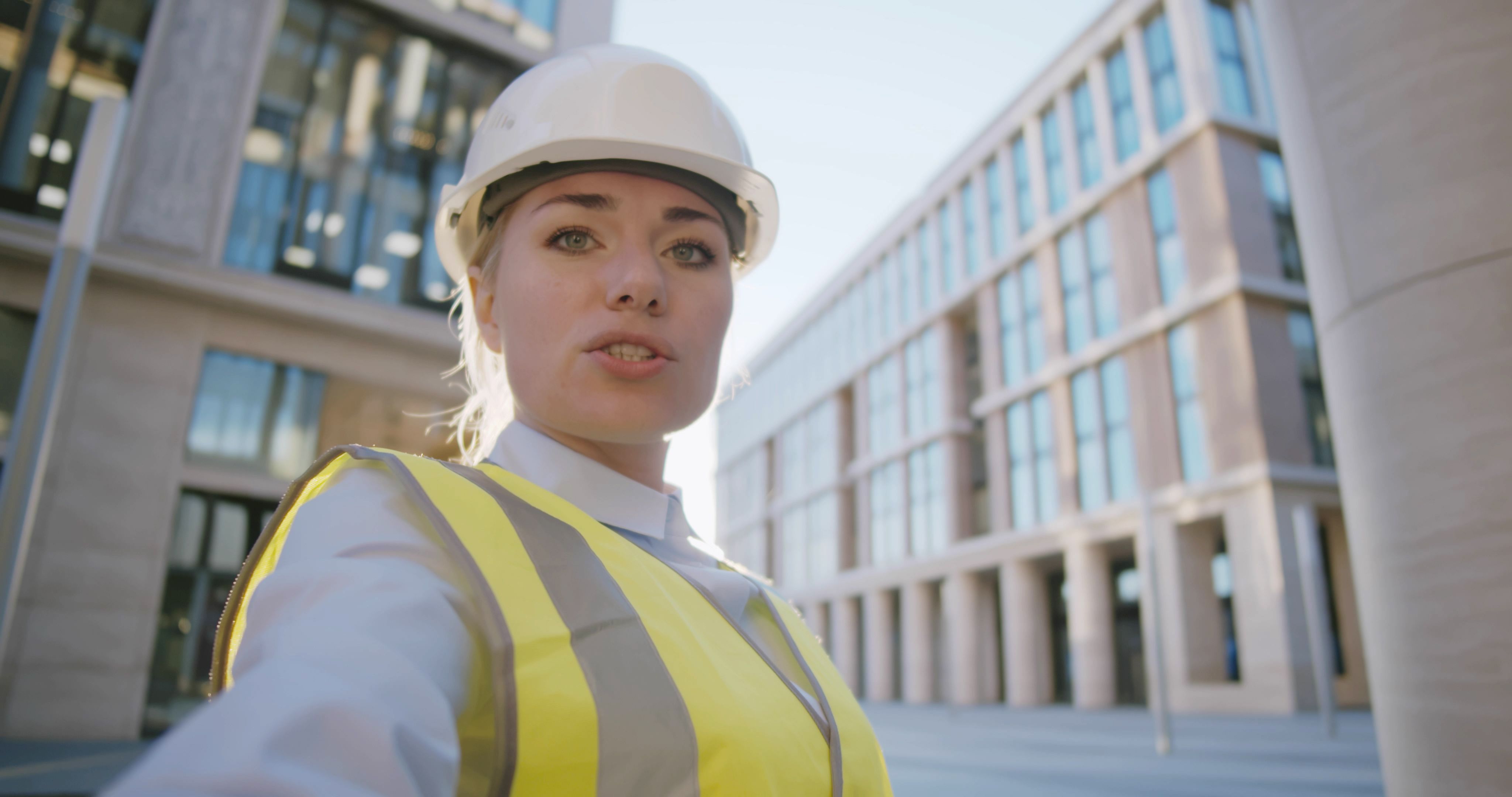 Female engineer in hardhat making video call to client standing outdoors at construction site Female engineer in hardhat making video call to client standing outdoors at construction site
