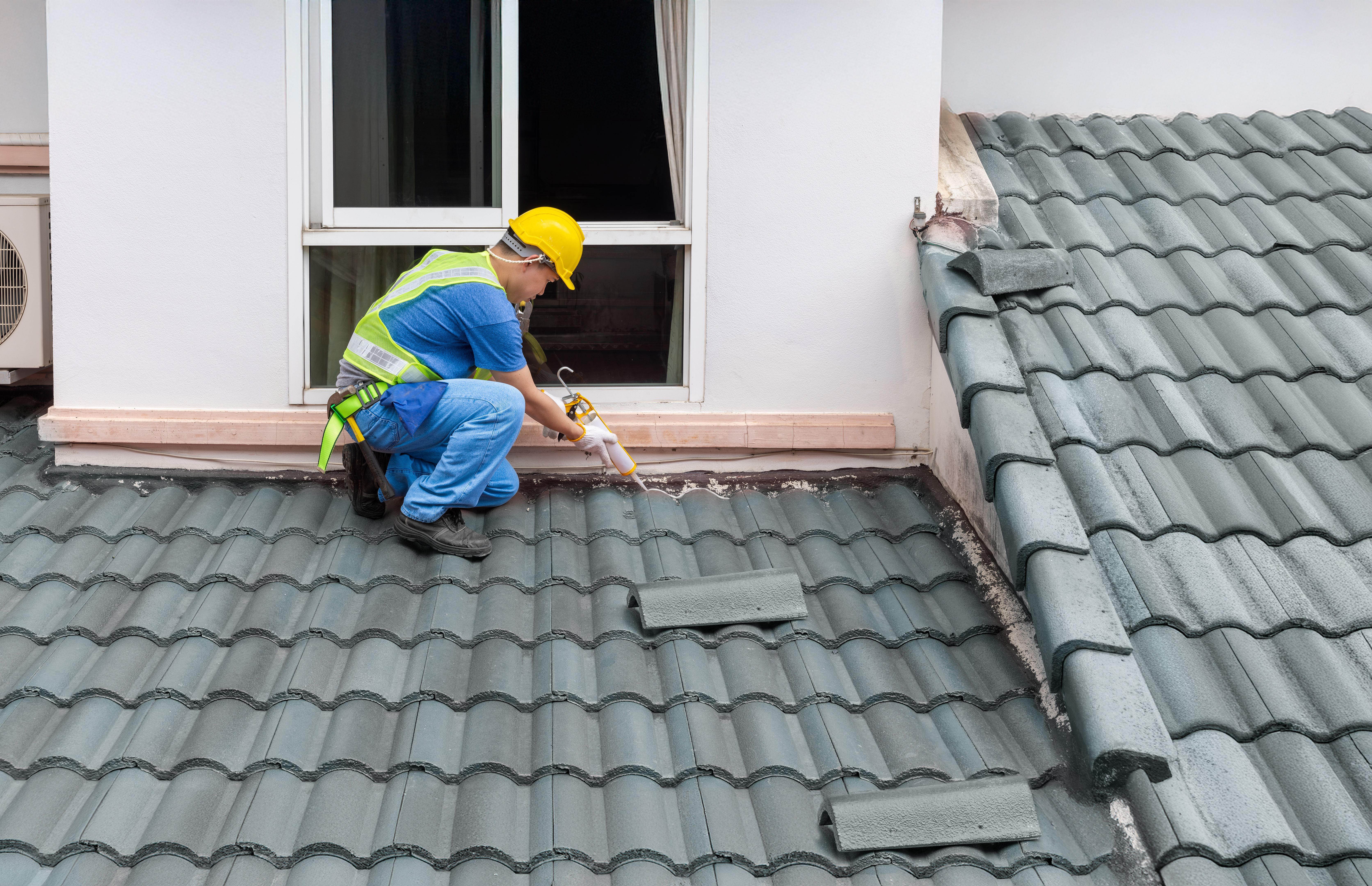 Construction worker using silicone sealant adhesive to fix crack of the old tile roof.