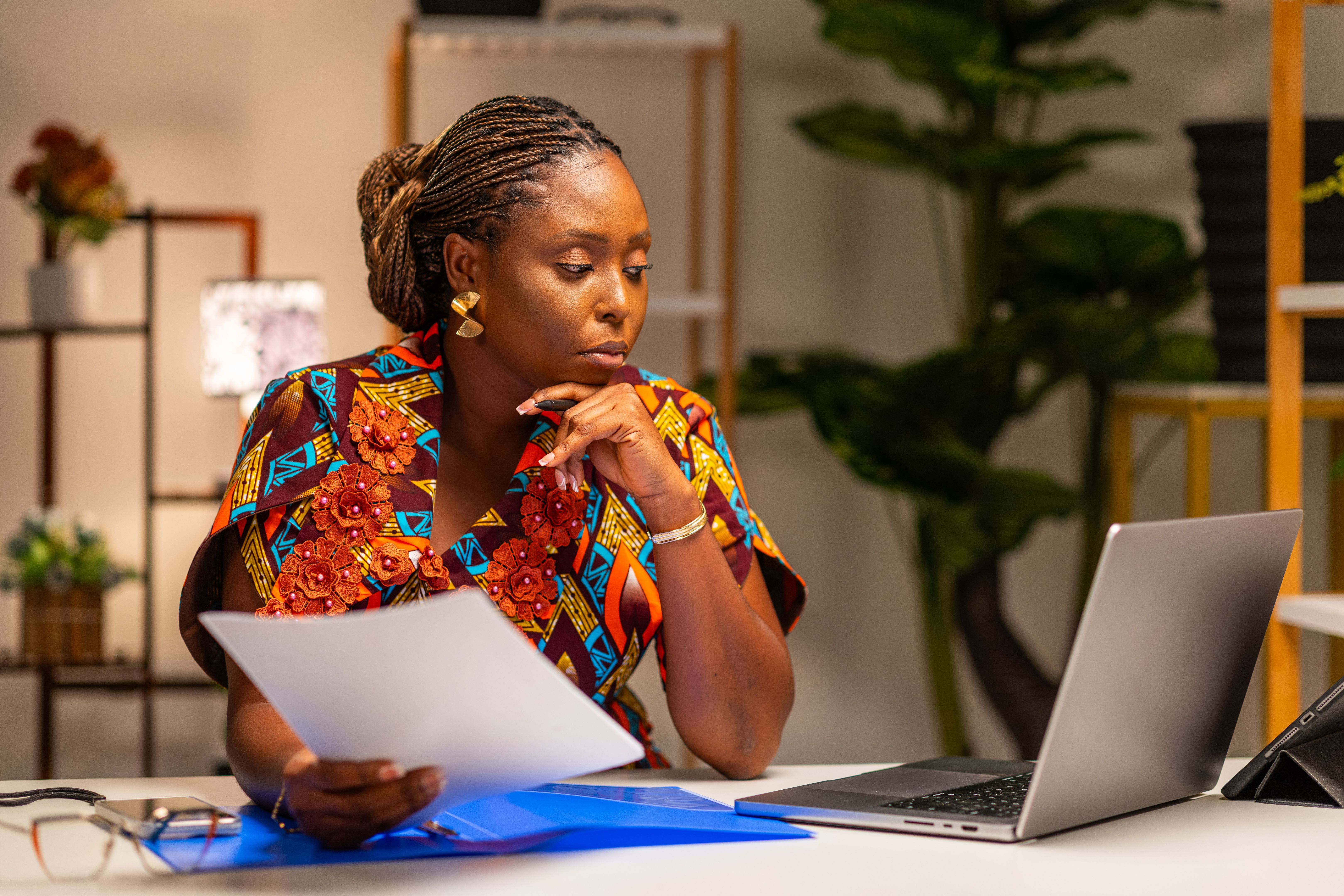 Focused African businesswoman reviewing documents while working on a laptop, accountant or analyst at work