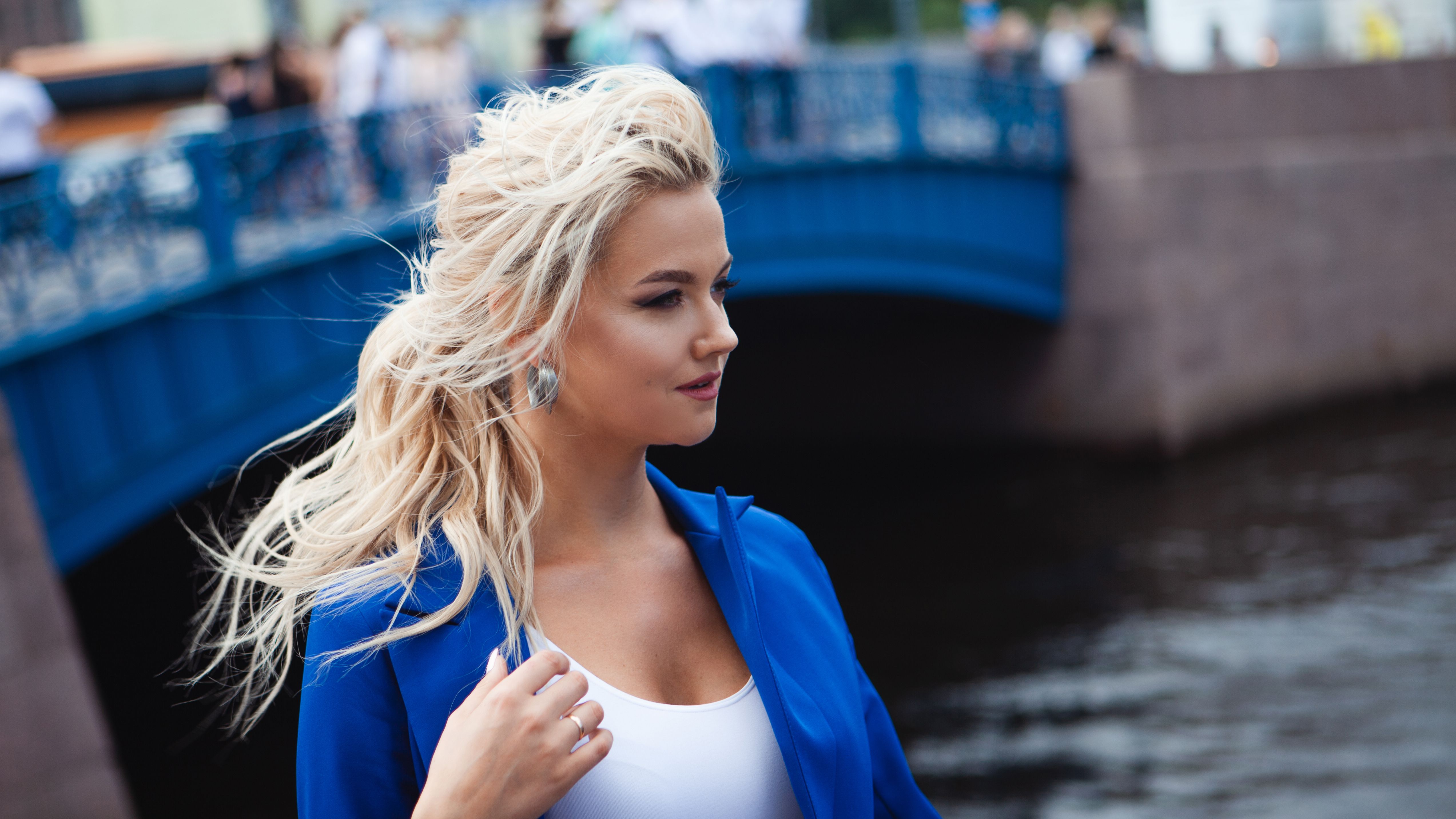 Portrait of a beautiful young woman, a blonde in a blue jacket on the background of the old blue bridge over the river.