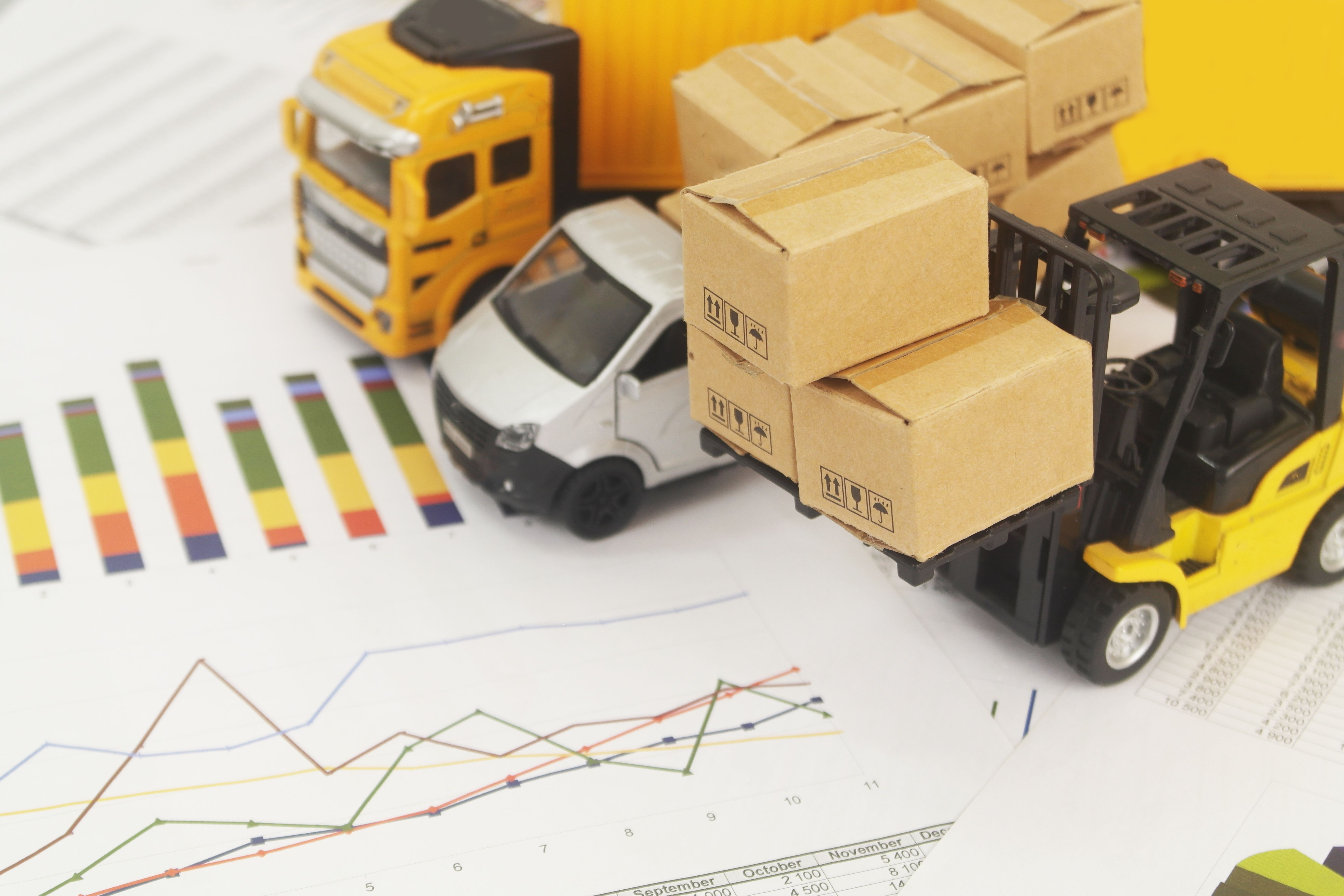 Lorry truck with cardboard boxes, container carrier and forklift on reports with financial figures.