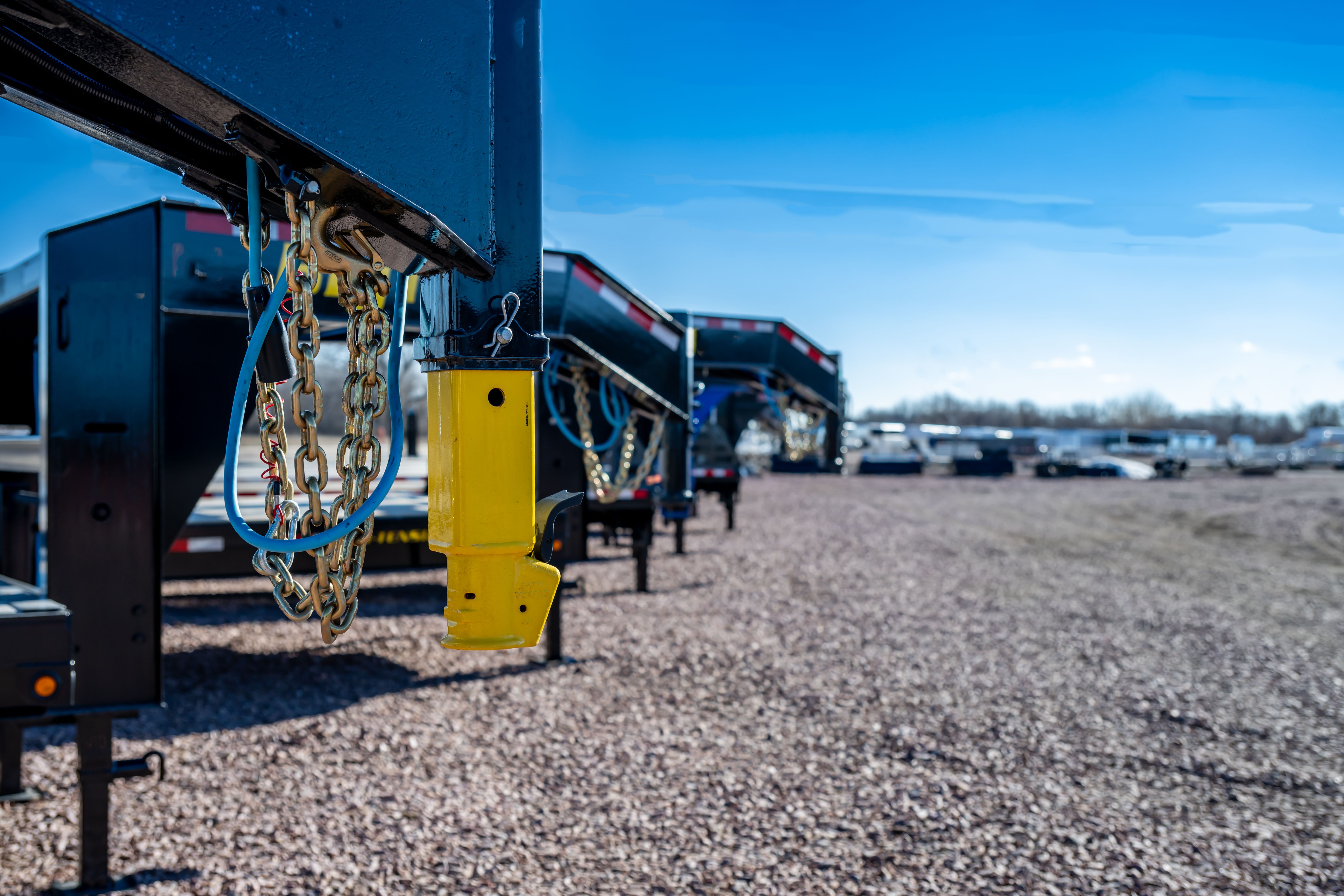 Selective focus on gooseneck trailer hitch with a row of flatbeds lined up.