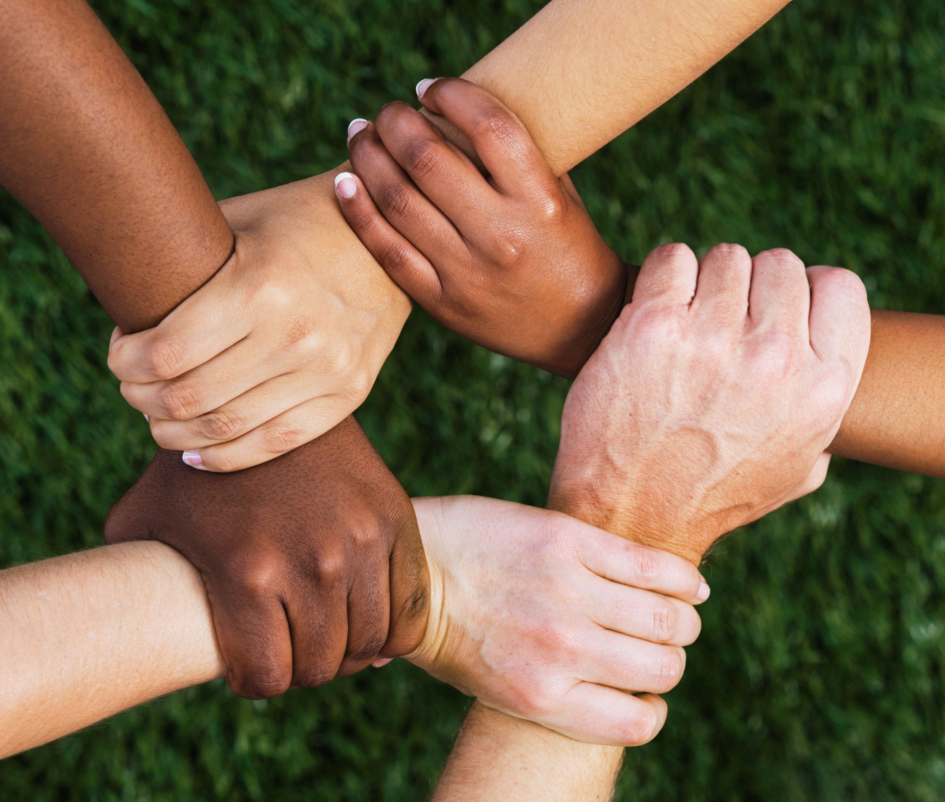 Diverse group of people with hands, wrists and arms interlinked, representing solidarity and teamwork