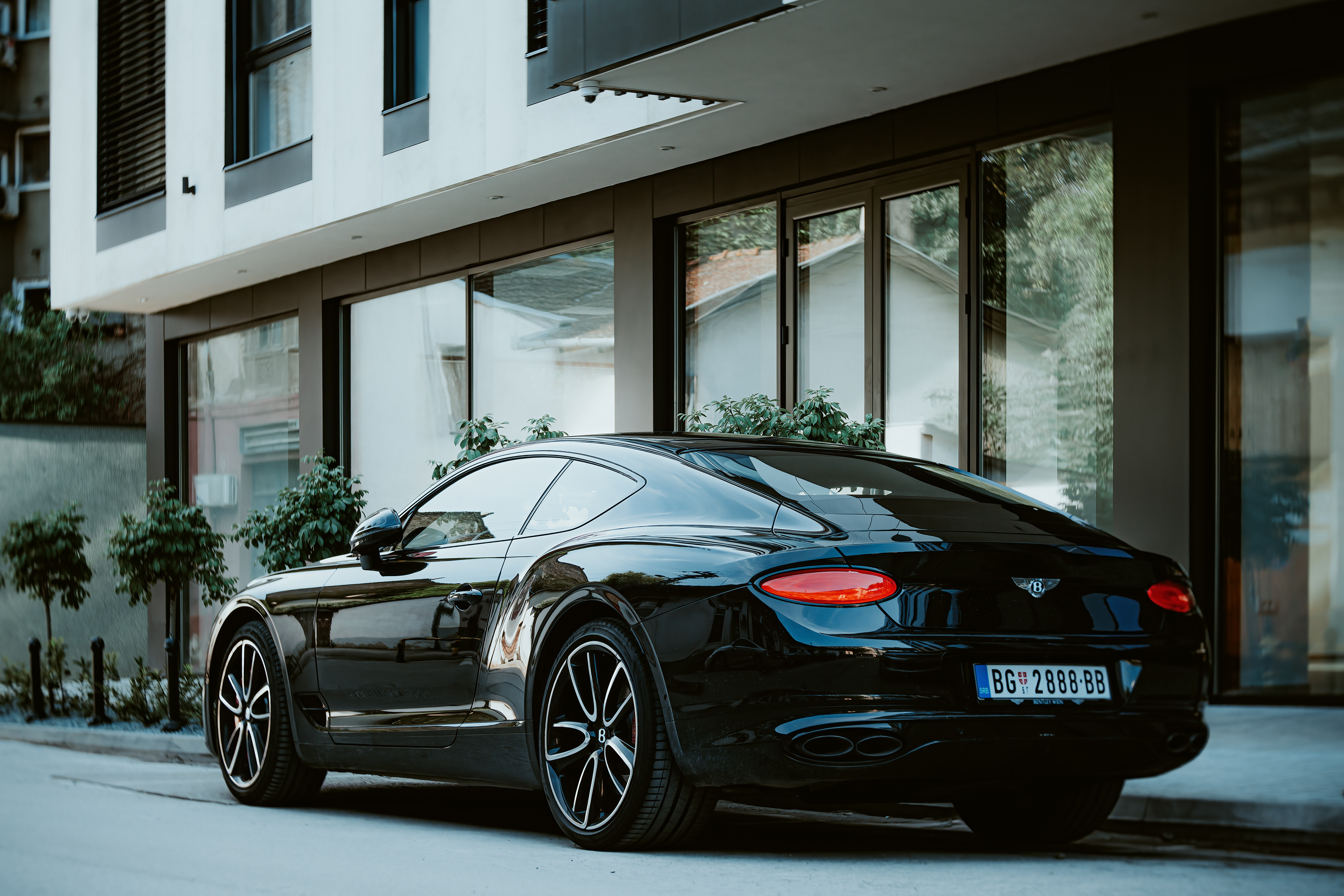 Bentley Continental GT W12 3 (third generation) is parked near newly constructed appartment building. Side-back view, vintage lens.