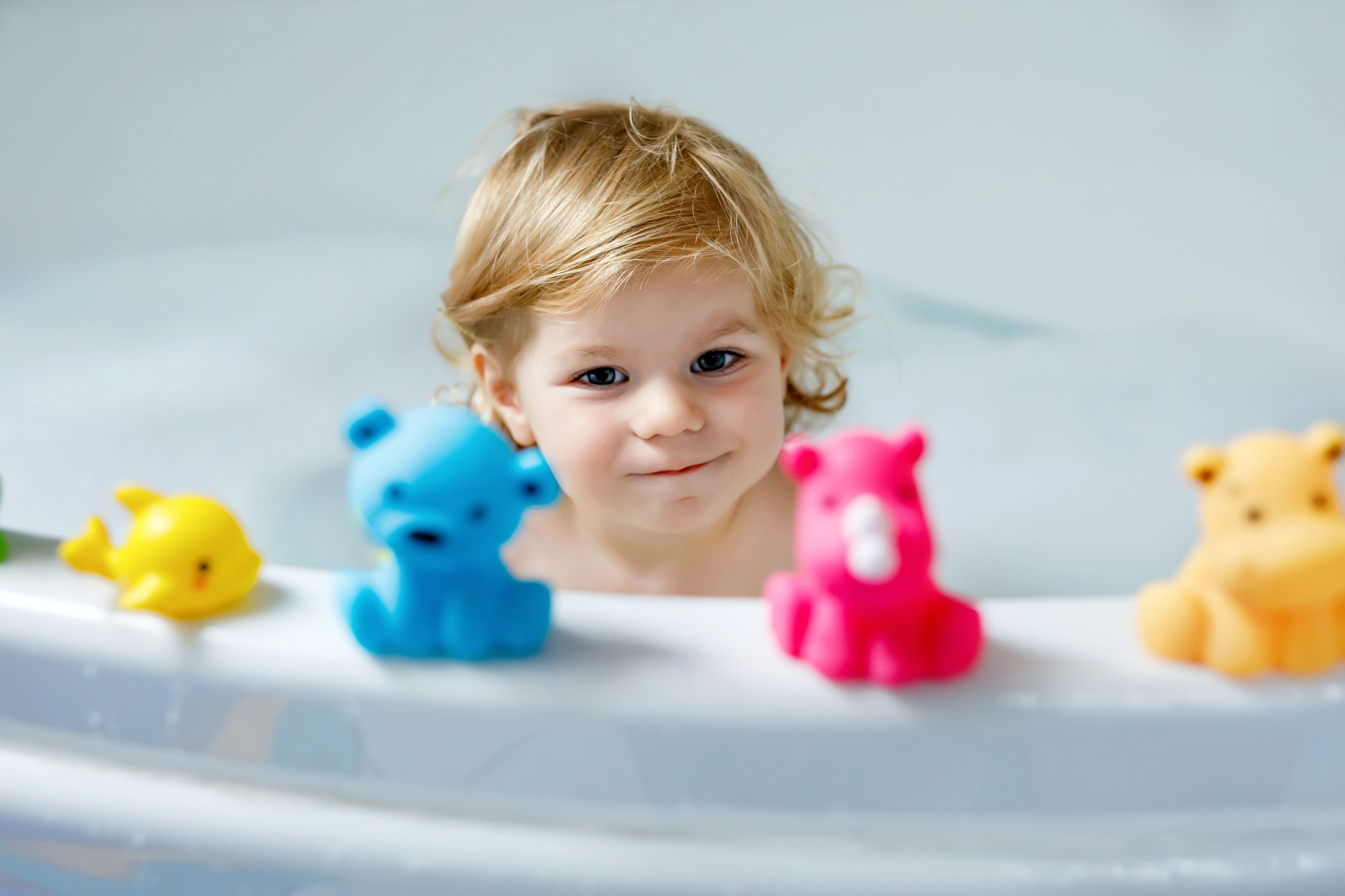 Adorable cute little toddler girl taking bath in bathtub. Happy healthy baby child playing with rubber gum toys and having fun. Washing, cleaning, hygiene for children.