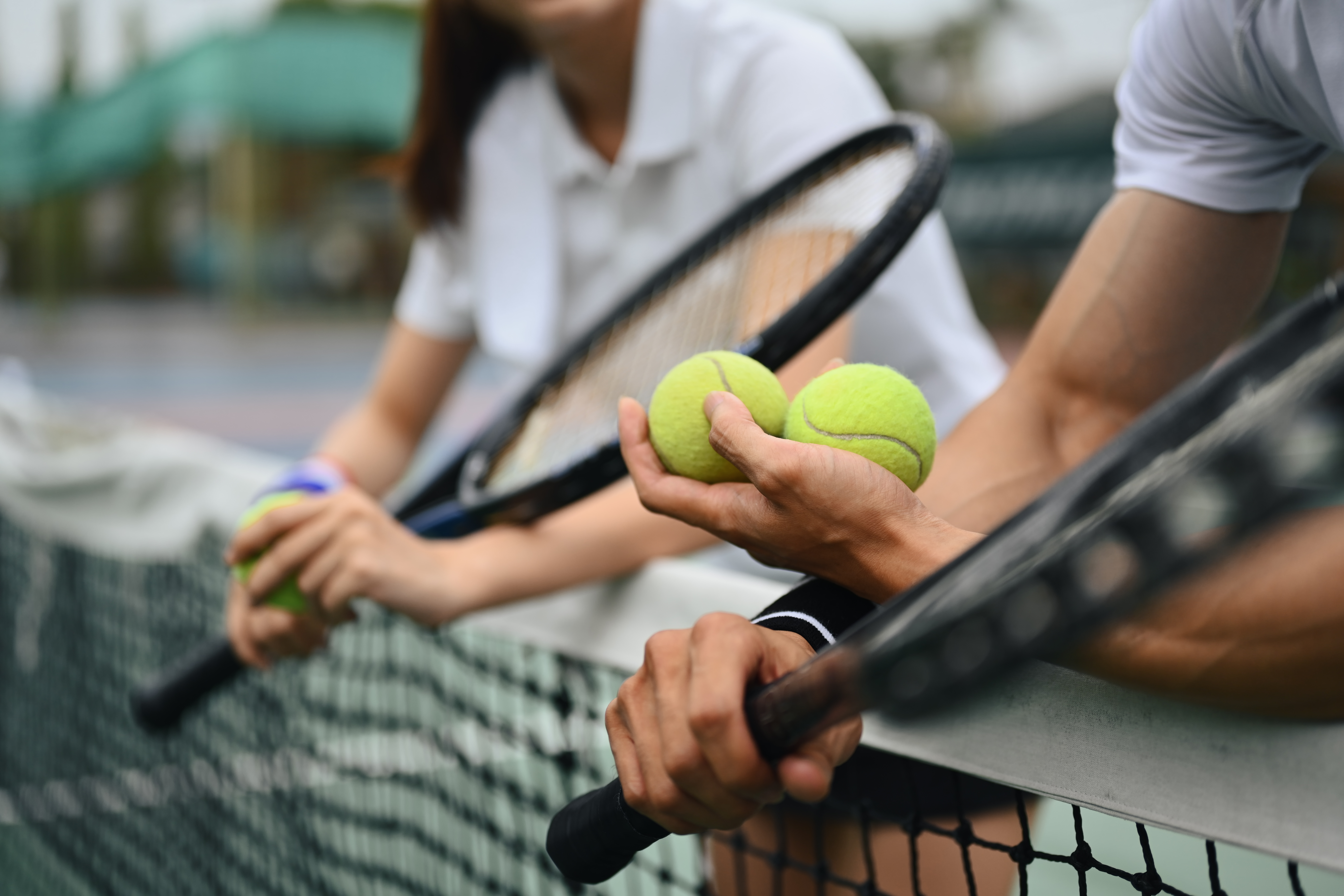 Cropped shot of male tennis coach hand holding balls, giving instructions to his student, standing by net at the court. Cropped shot of male tennis coach hand holding balls, giving instructions to his student, standing by net at the court.