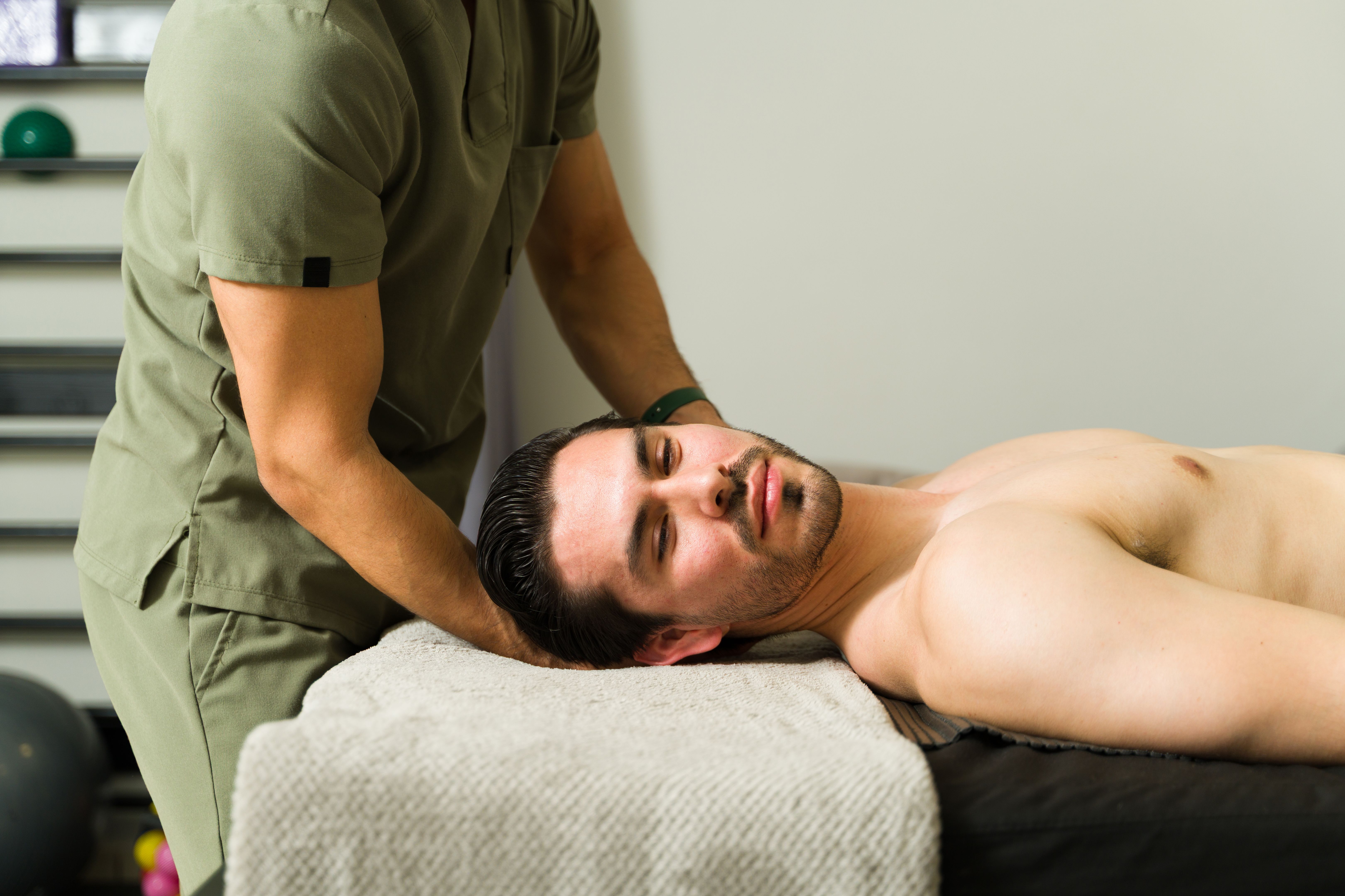 Professional physiotherapist massaging neck of male patient lying on massage table, receiving manual therapy treatment