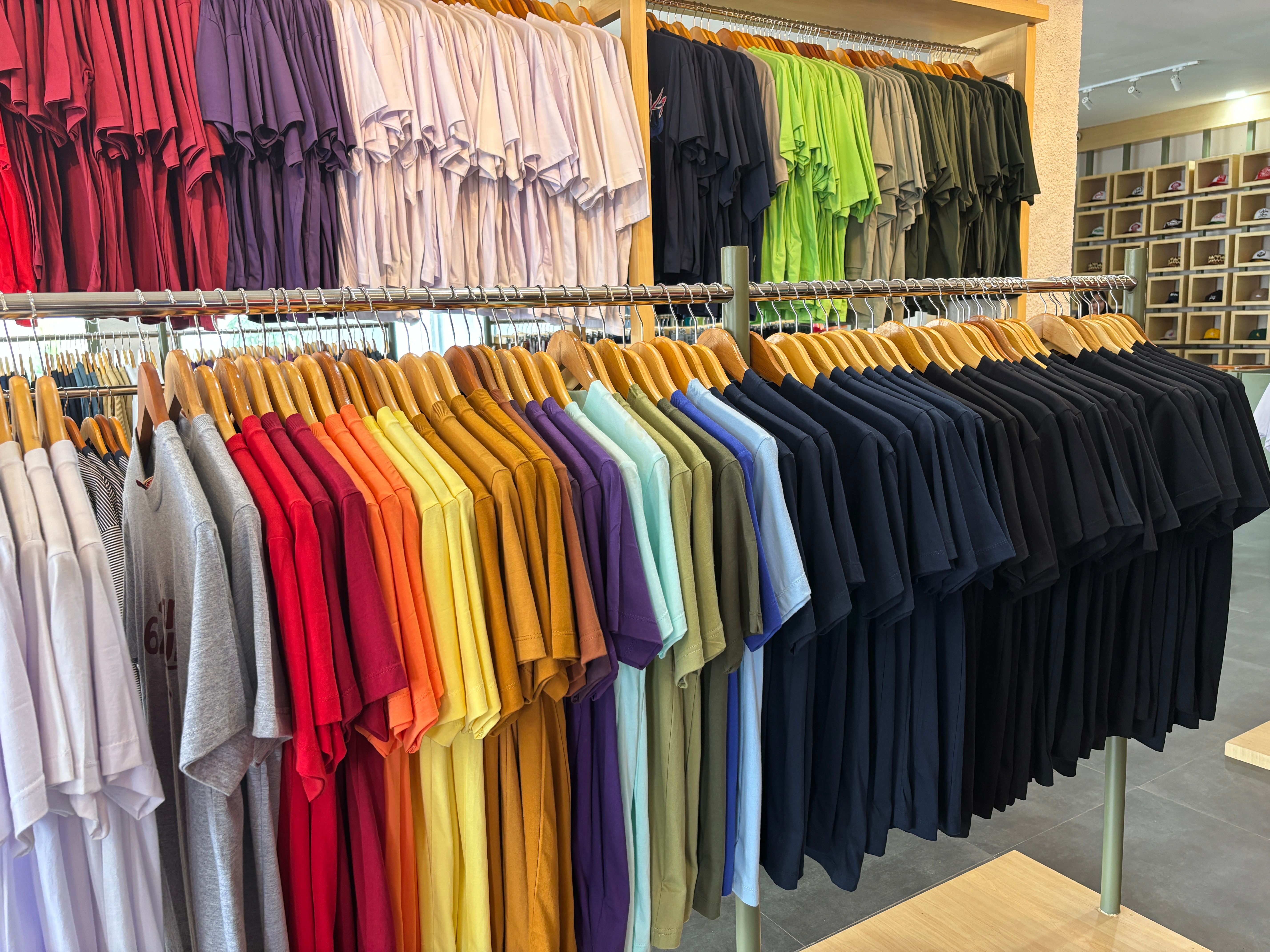 A clothing store display various  t-shirts in a wide spectrum of colors, neatly hung on wooden hangers