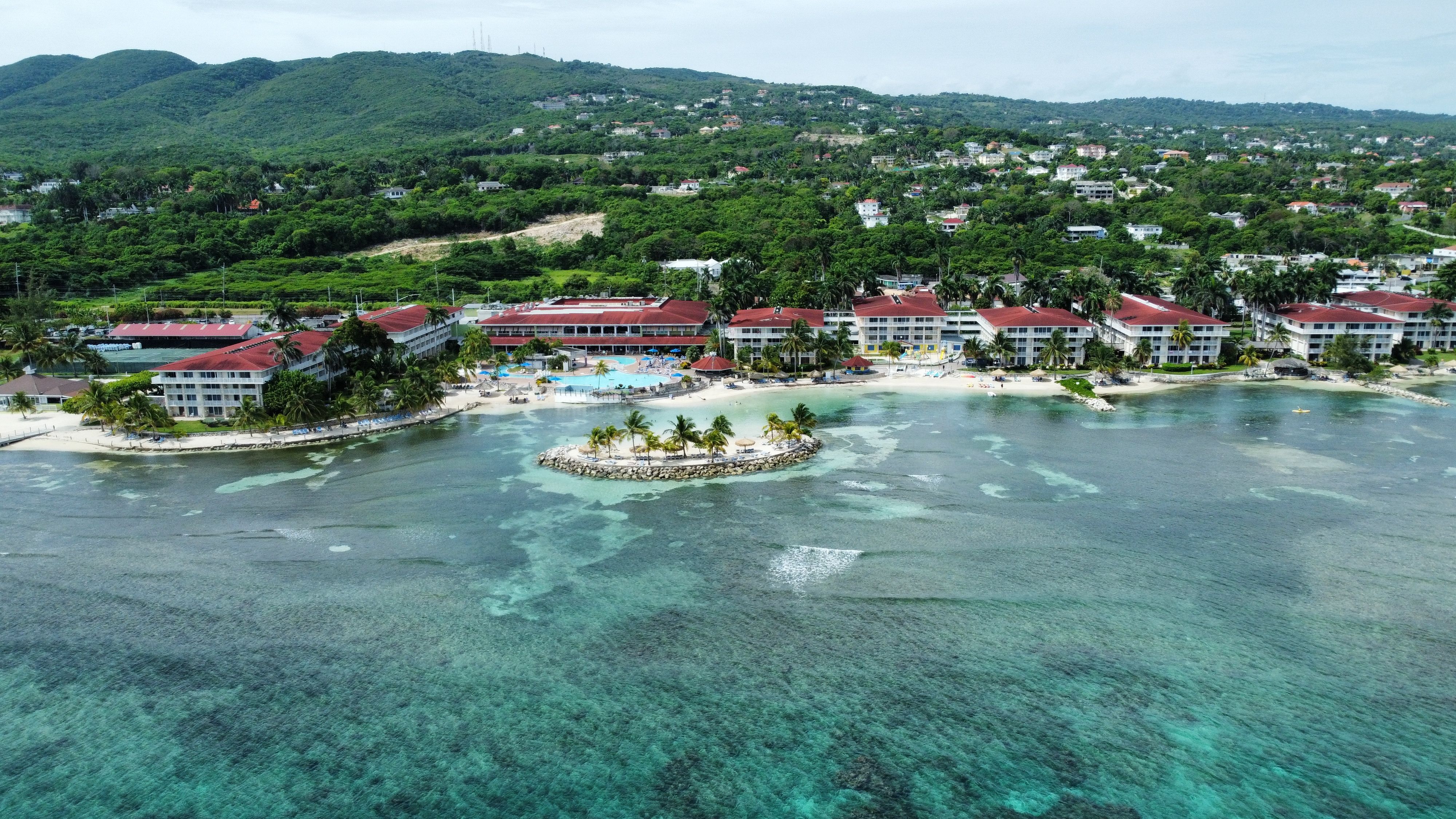 Aerial of hotels on a beach covered with greenery against a turquoise sea in Montego Bay, Jamaica