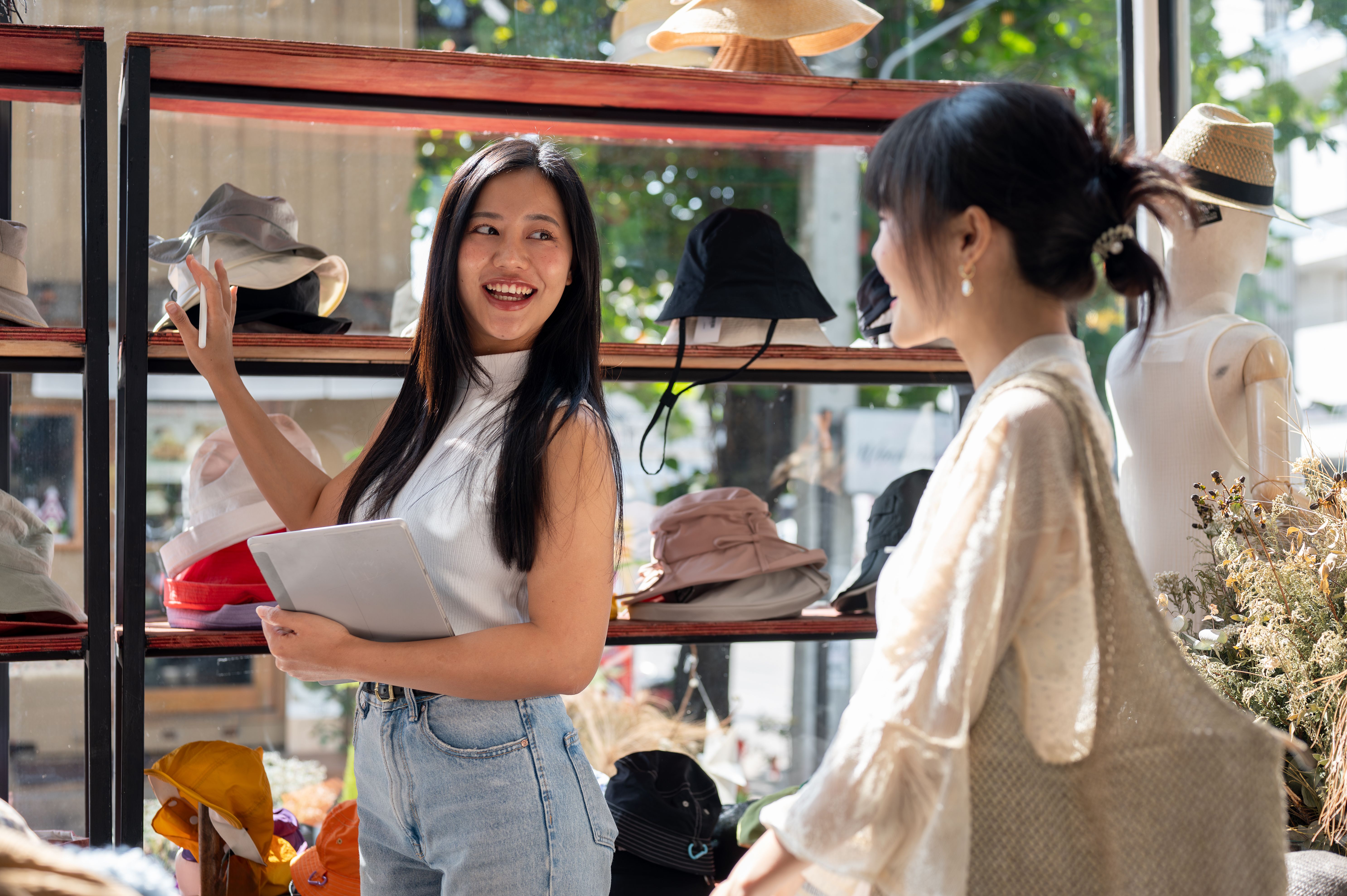 Friendly, attractive Asian female shop assistant is recommending new items on a shelf to a customer.