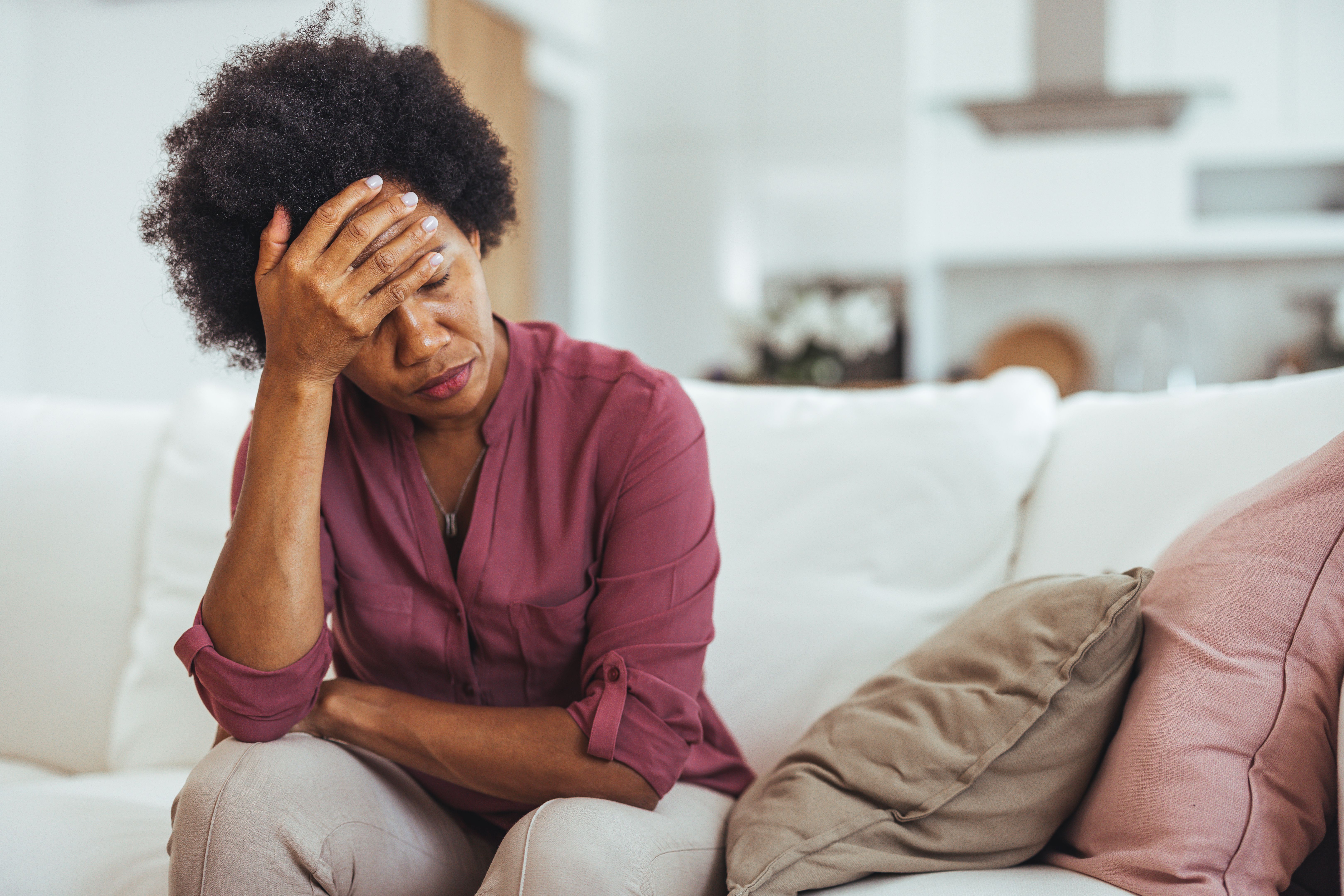 Stressed Woman Sitting On Sofa Holding Head In Hand