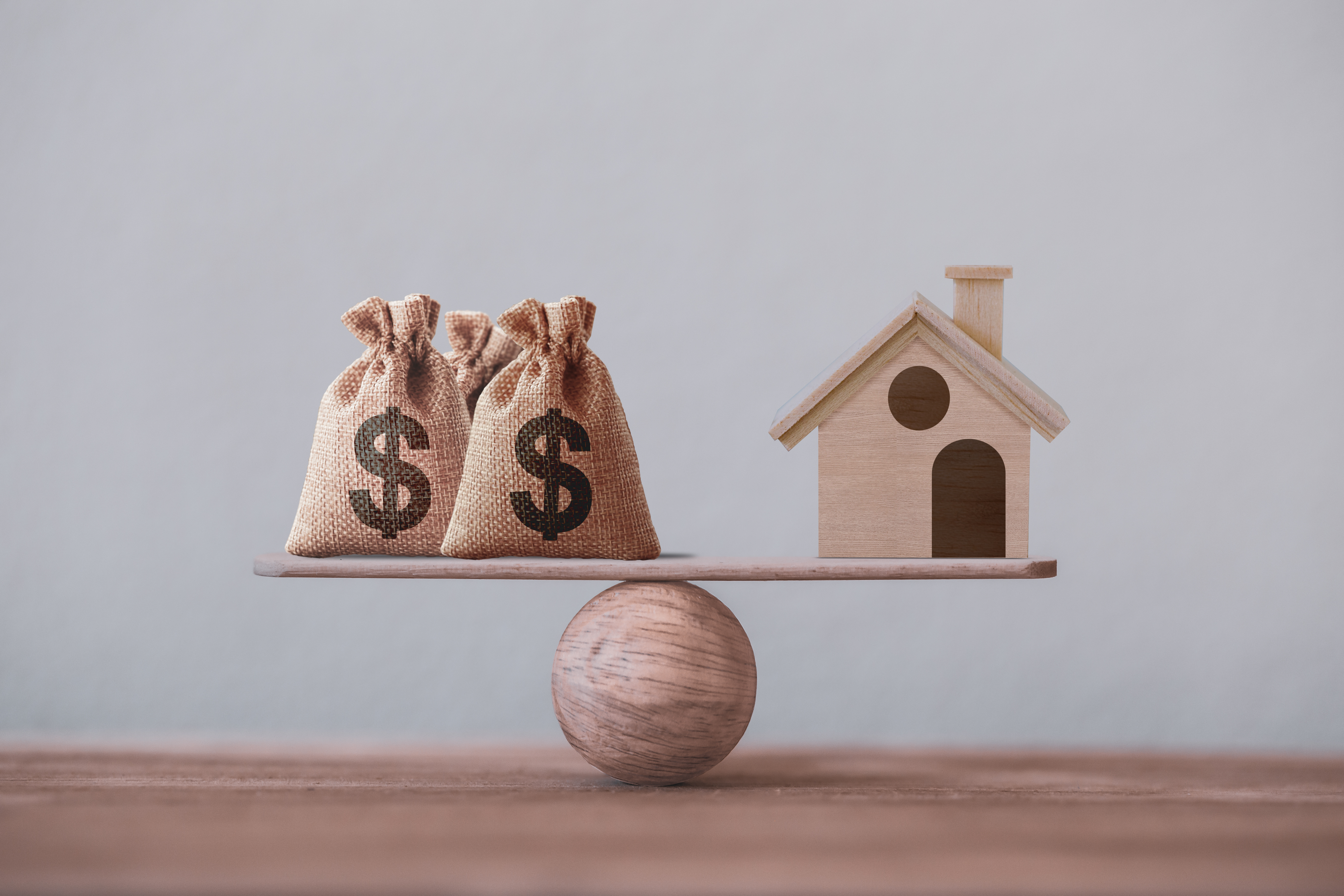 US dollar hessian bags with house paper model on a wood balance scale. Home loan, reverse mortgage concept, Depicts a homeowner or a borrower turns properties into cash US dollar hessian bags with house paper model on a wood balance scale. Home loan, reverse mortgage concept, Depicts a homeowner or a borrower turns properties into cash
