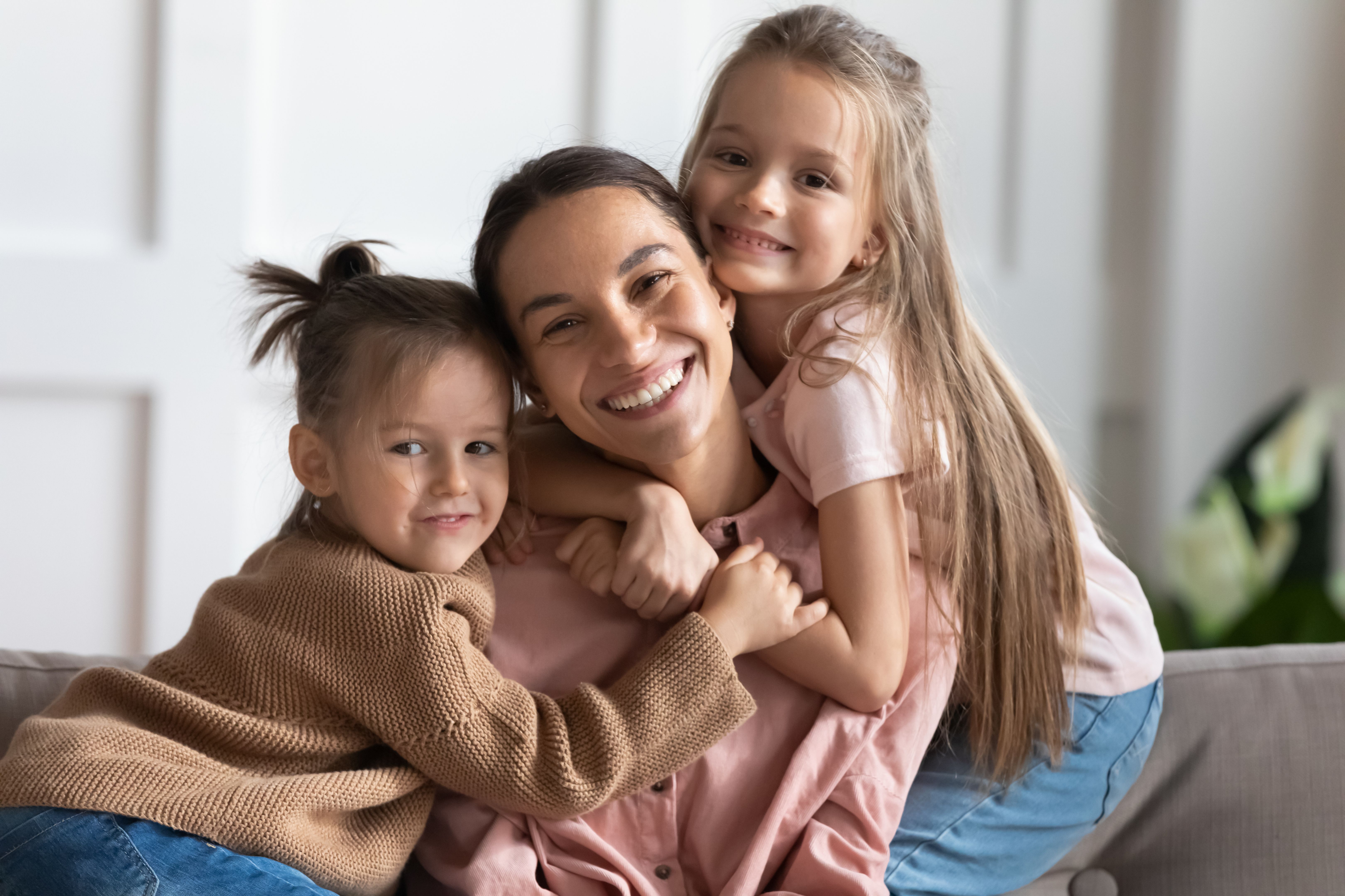 Little beautiful daughters hug mom, family smiling looking at camera