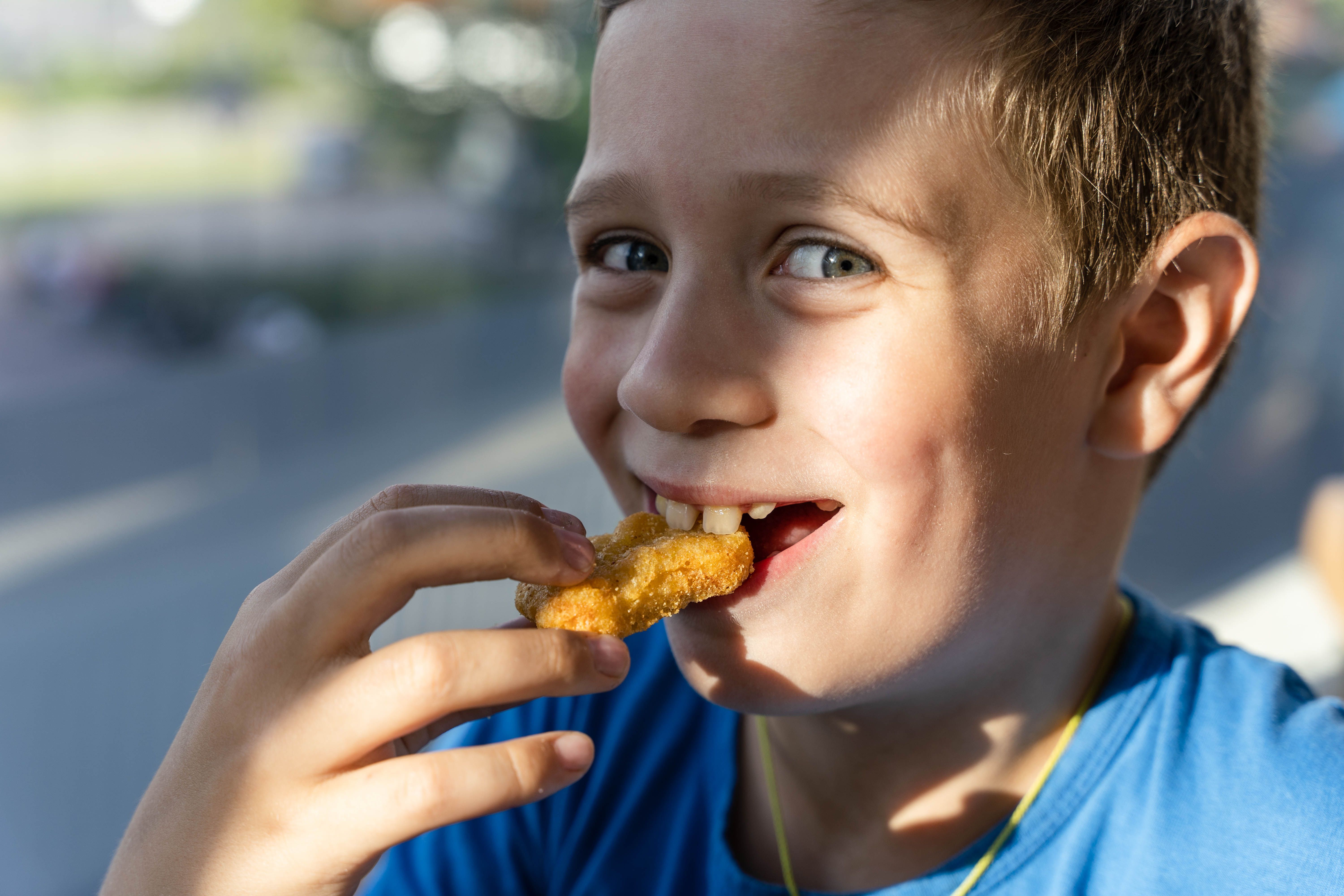 A boy with a pleasant smile enjoys eating delicious nuggets