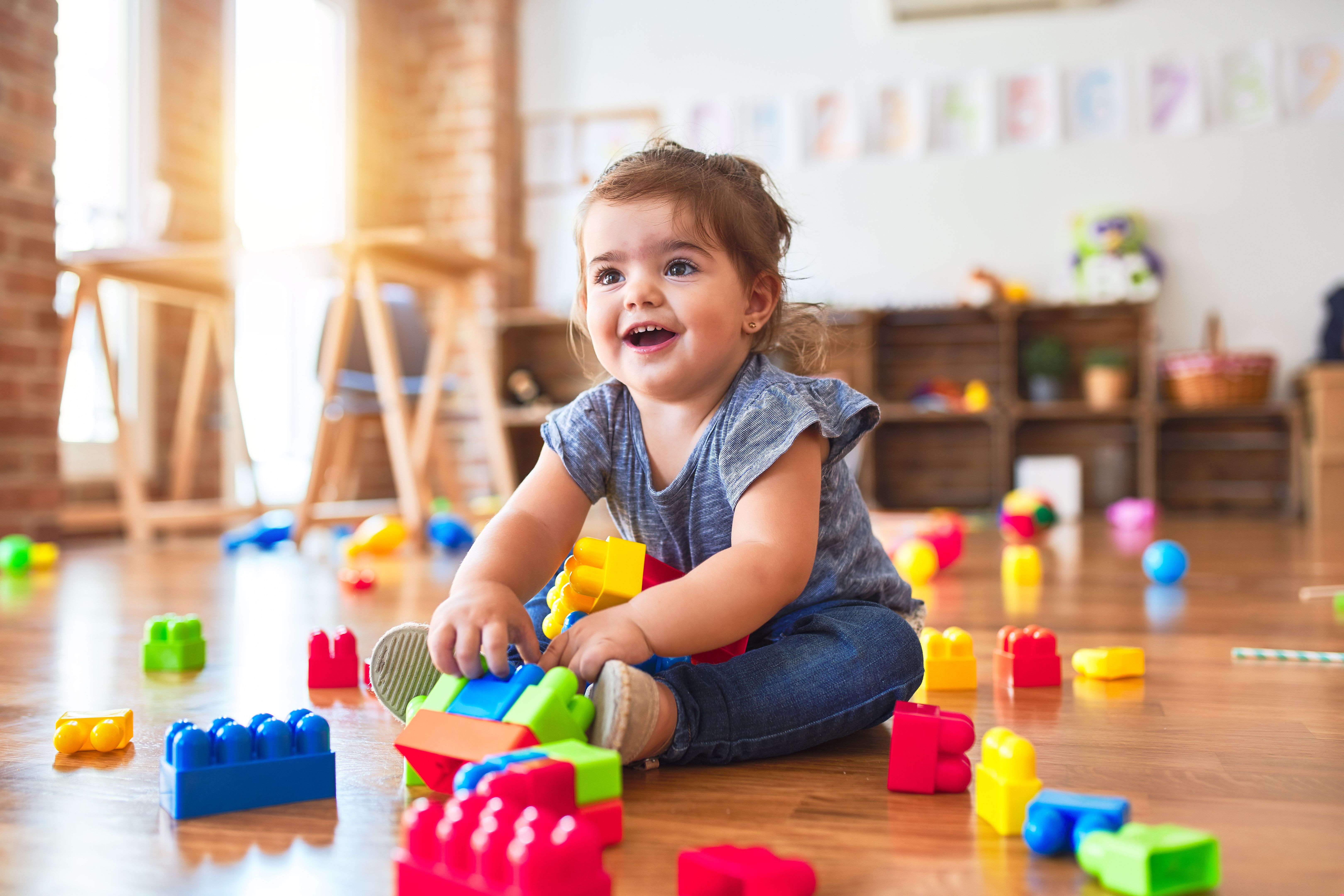 Beautiful toddler sitting on the floor playing with building blocks toys at kindergarten Beautiful toddler sitting on the floor playing with building blocks toys at kindergarten