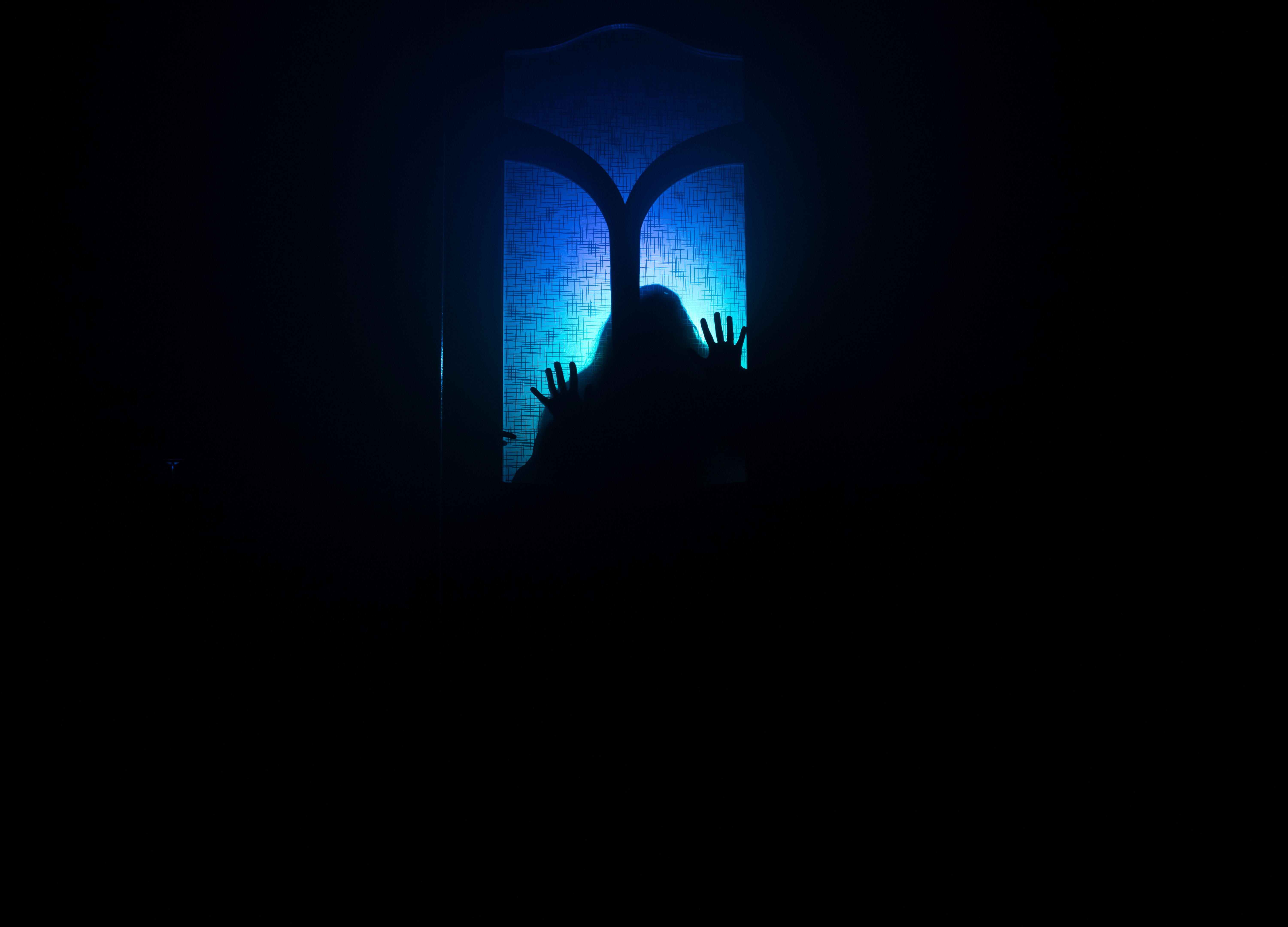 Silhouette of an unknown shadow figure on a door through a closed glass door. The silhouette of a human in front of a window at night. Scary scene halloween concept of blurred silhouette of maniac.