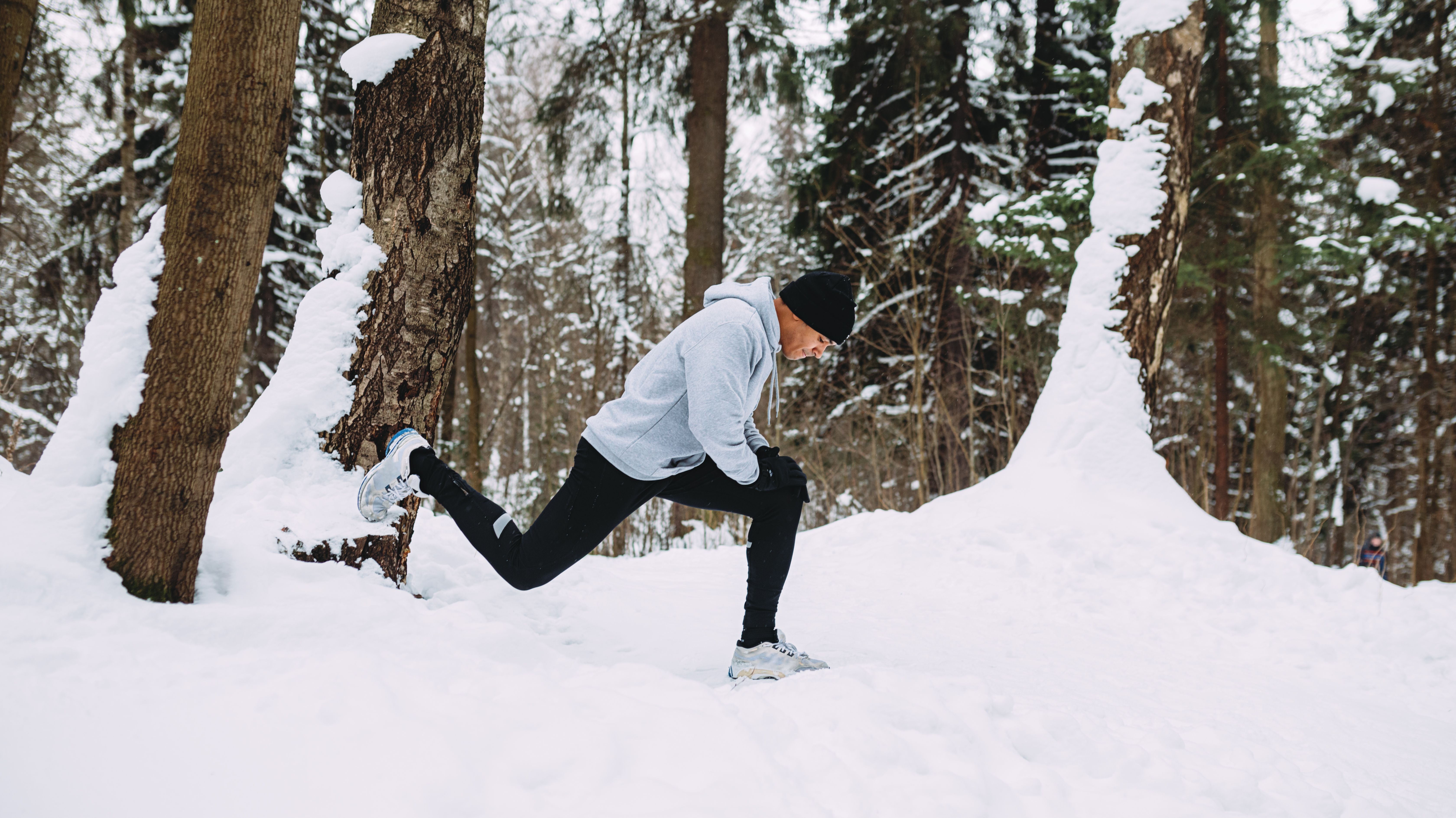 Corridore che fa esercizi di stretching in una foresta di neve Corridore che fa esercizi di stretching in una foresta di neve