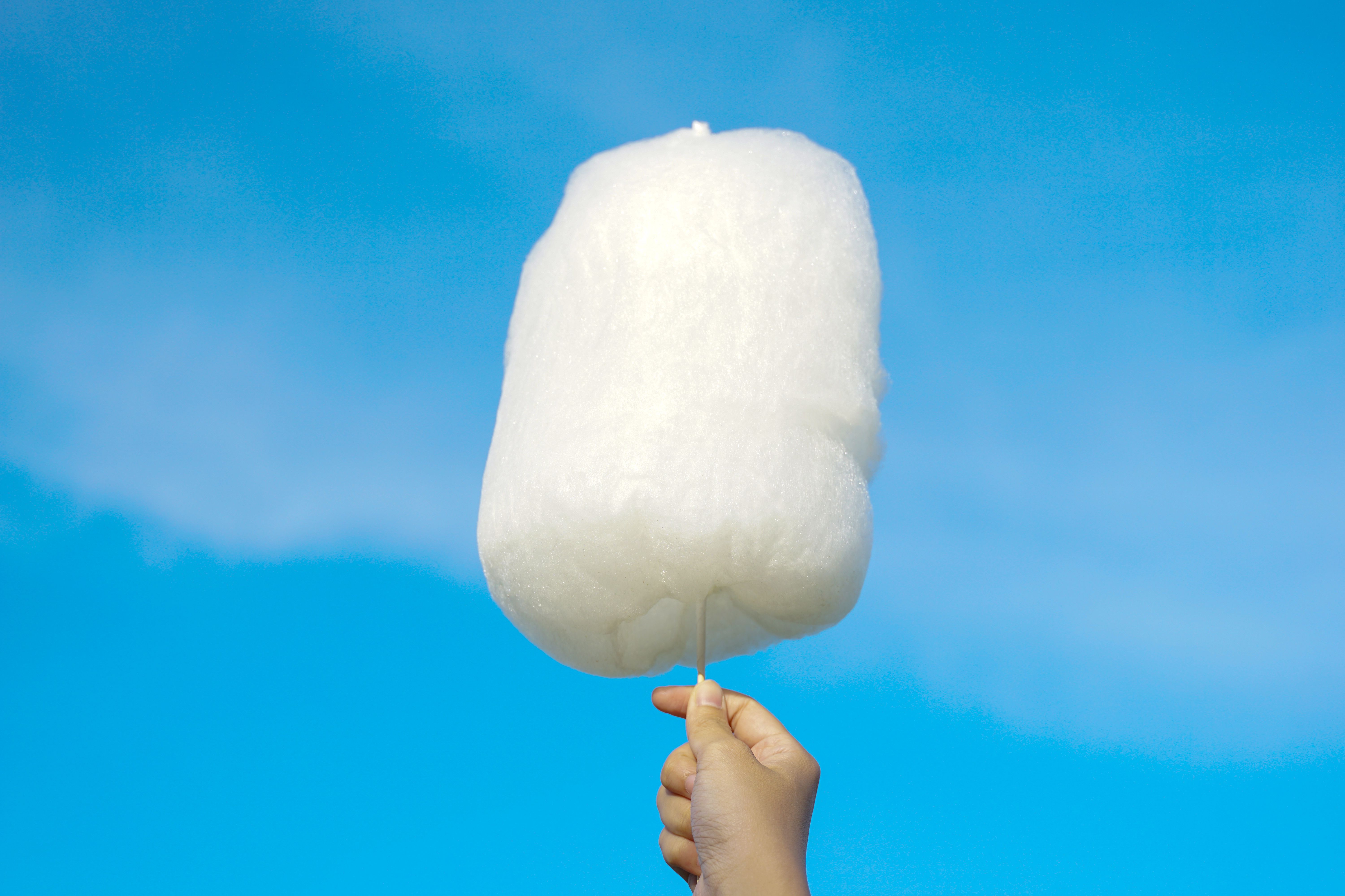 holding white cotton candy on sky background. Cotton candy made from sugar spun into thin noodles. Like a cloud, many colors depending on the color. Soft and selective focus.