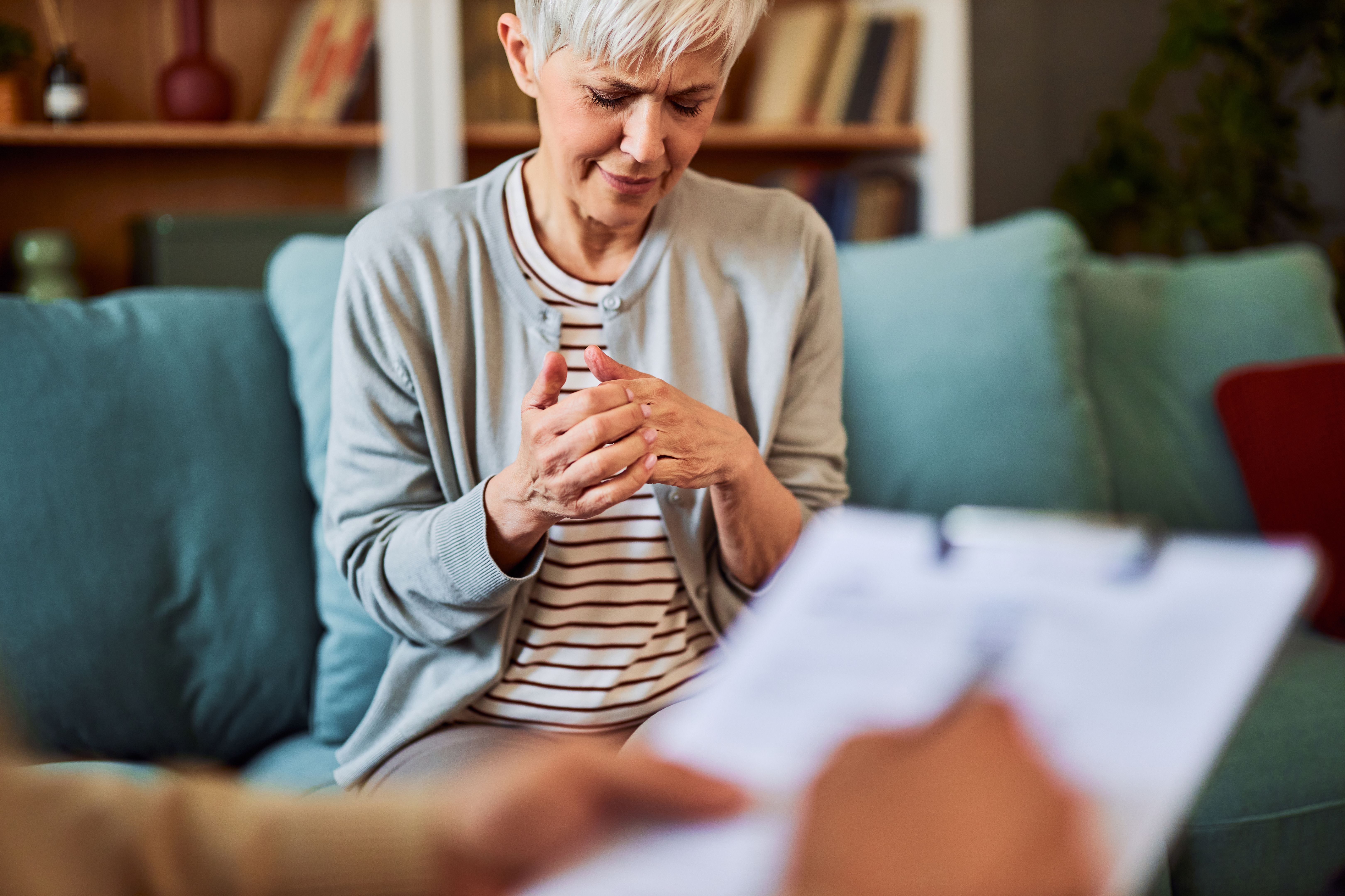 A depressed mature woman in despair fidgeting with her fingers with her eyes closed while sitting in the doctor's office