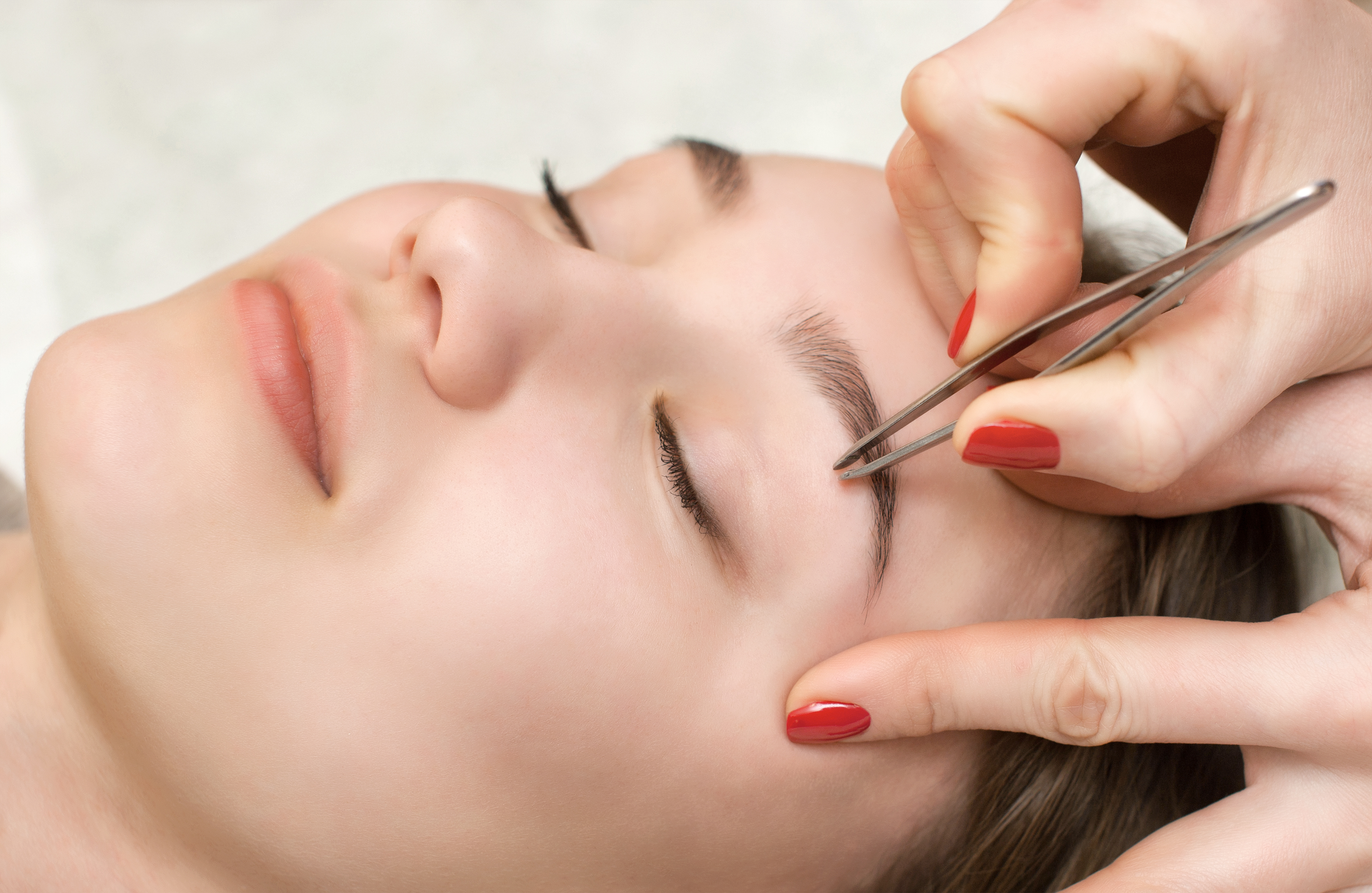The make-up artist plucks her eyebrows from a young woman in a beauty salon. Professional skin care and make-up.