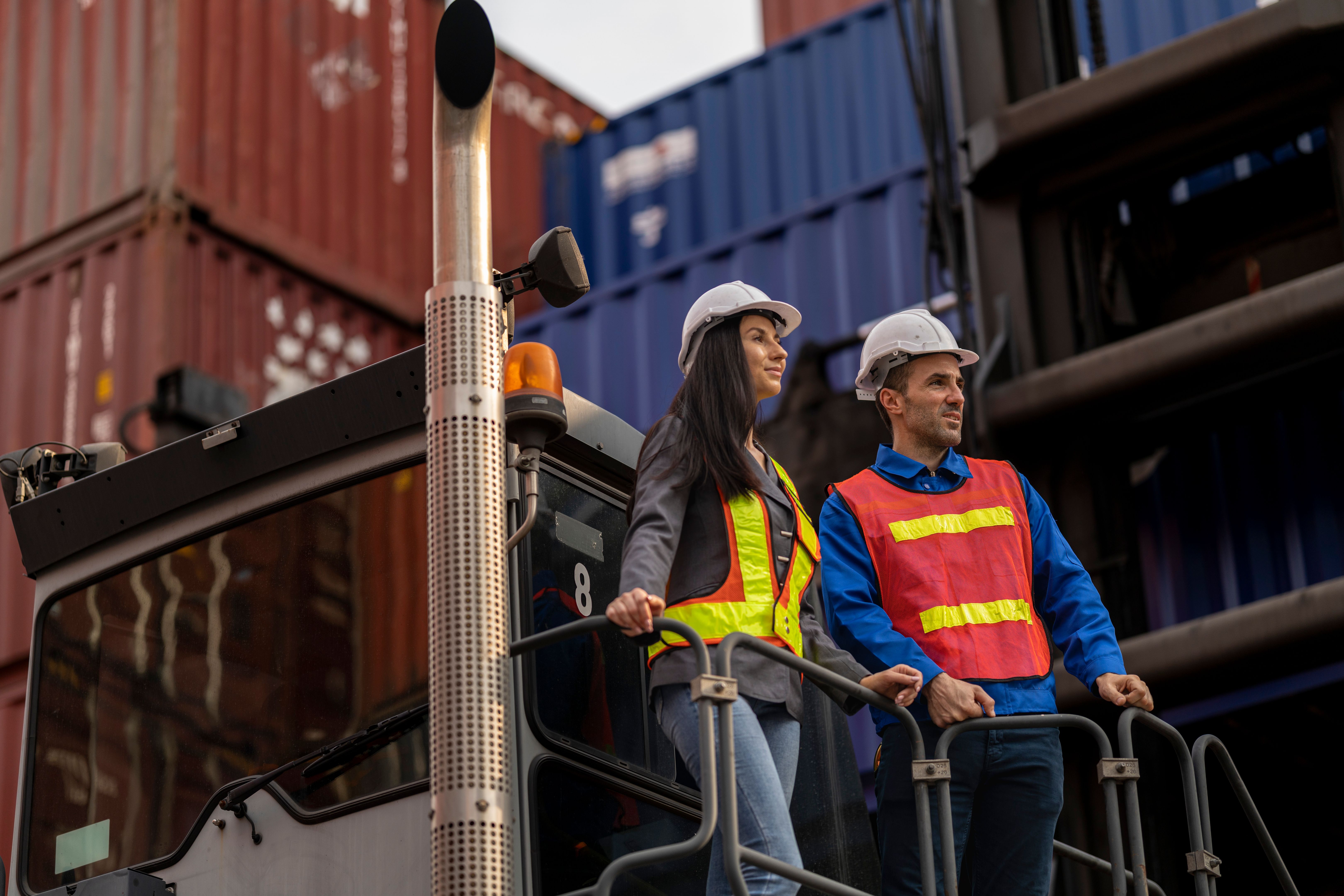 Two logistics workers man and woman discuss operations at a busy shipping container yard. successful coordination in freight, transportation, and supply chain operations