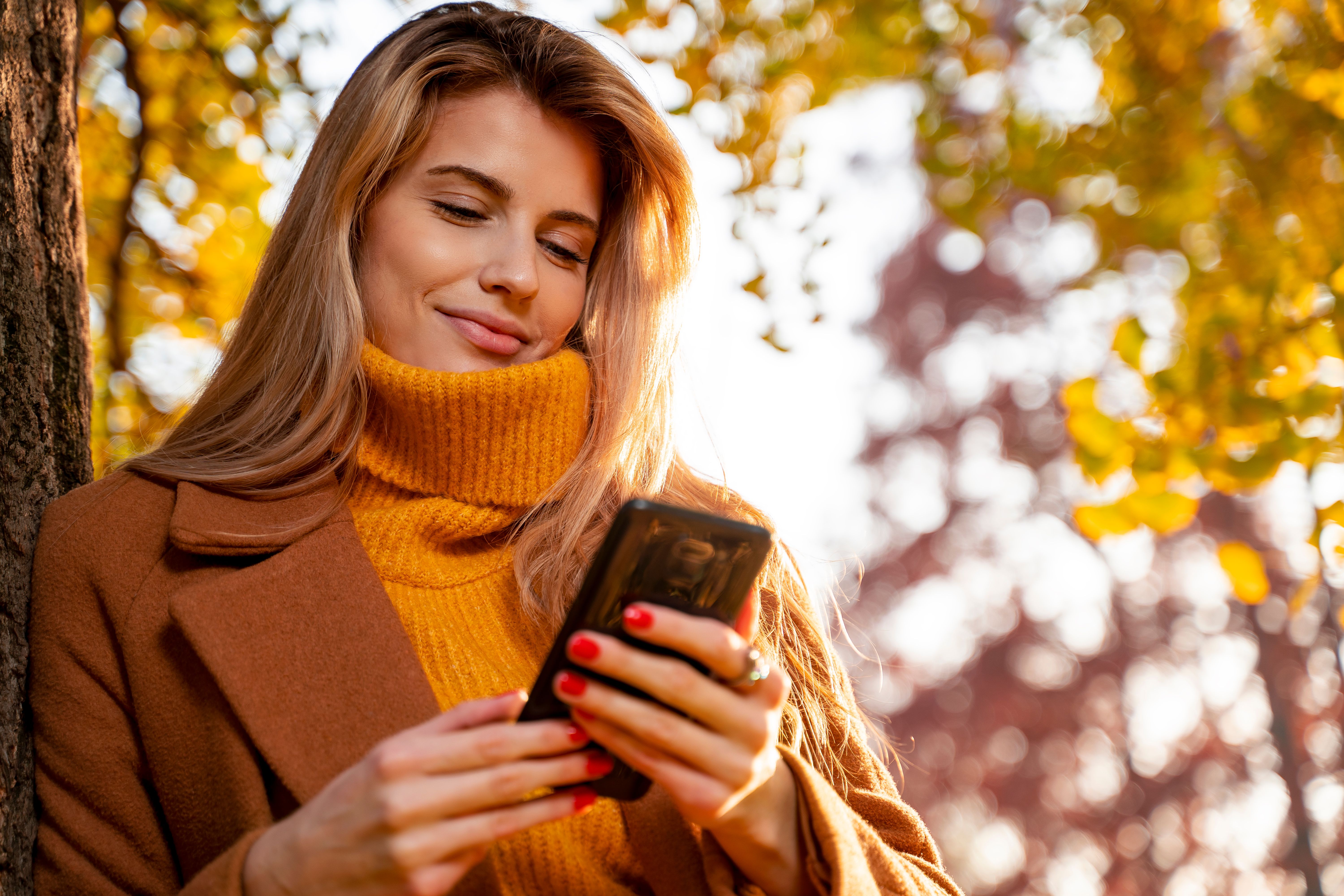 Pretty blonde in fall time in park using smartphone