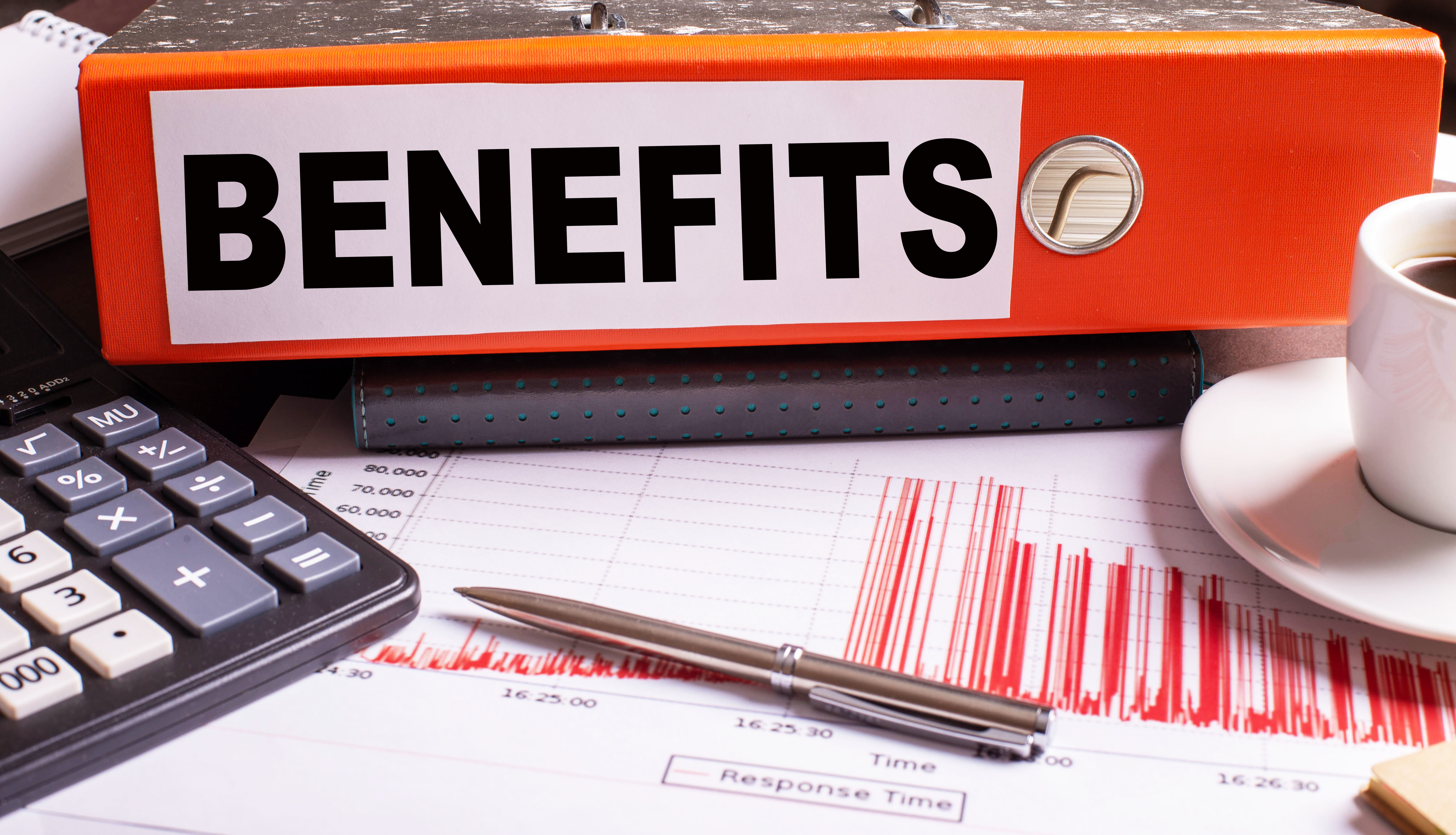 The word BENEFITS written on a paper folder next to a calculator and pen