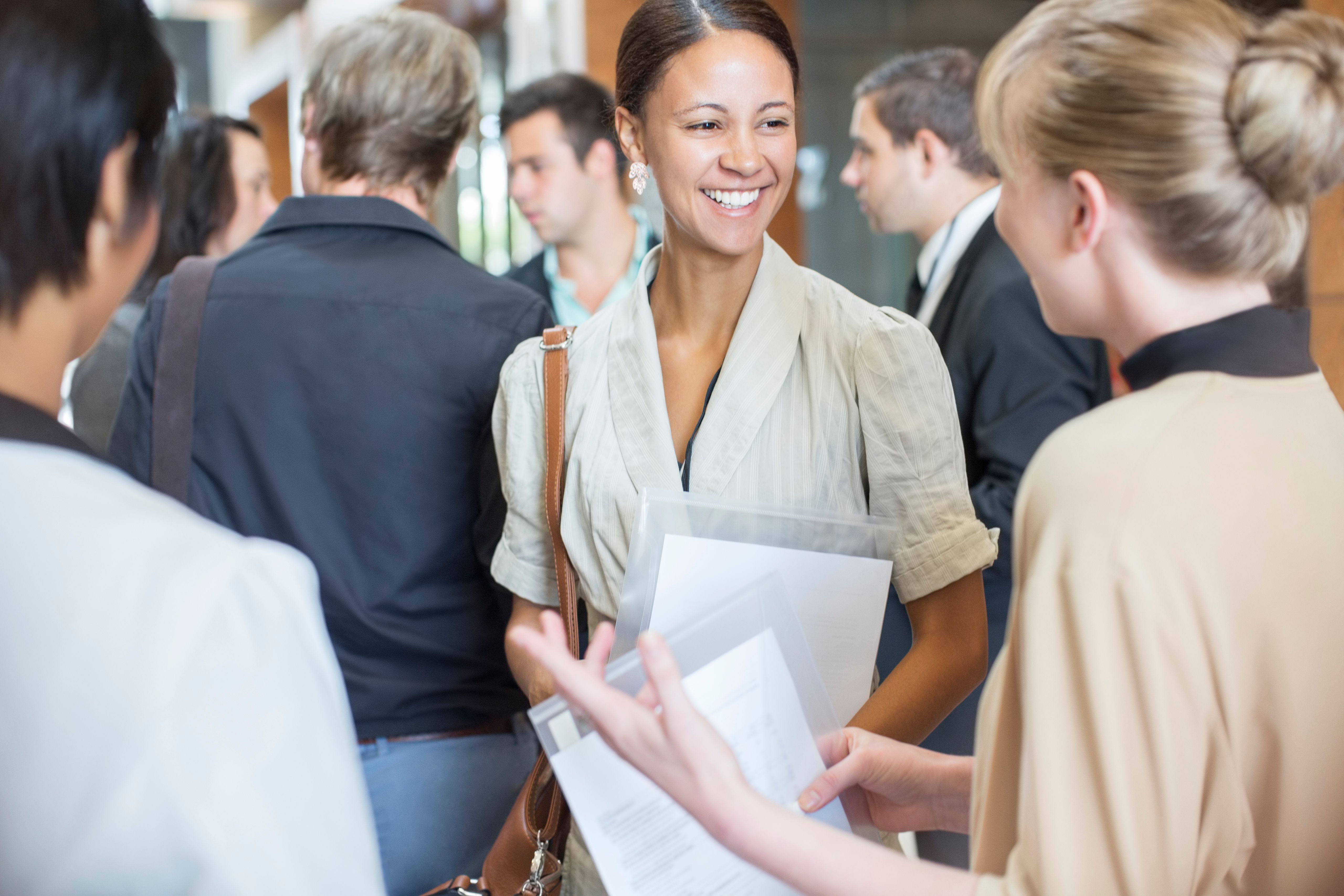 Portrait of two smiling women holding files and talking, standing in crowded lobby Portrait of two smiling women holding files and talking, standing in crowded lobby