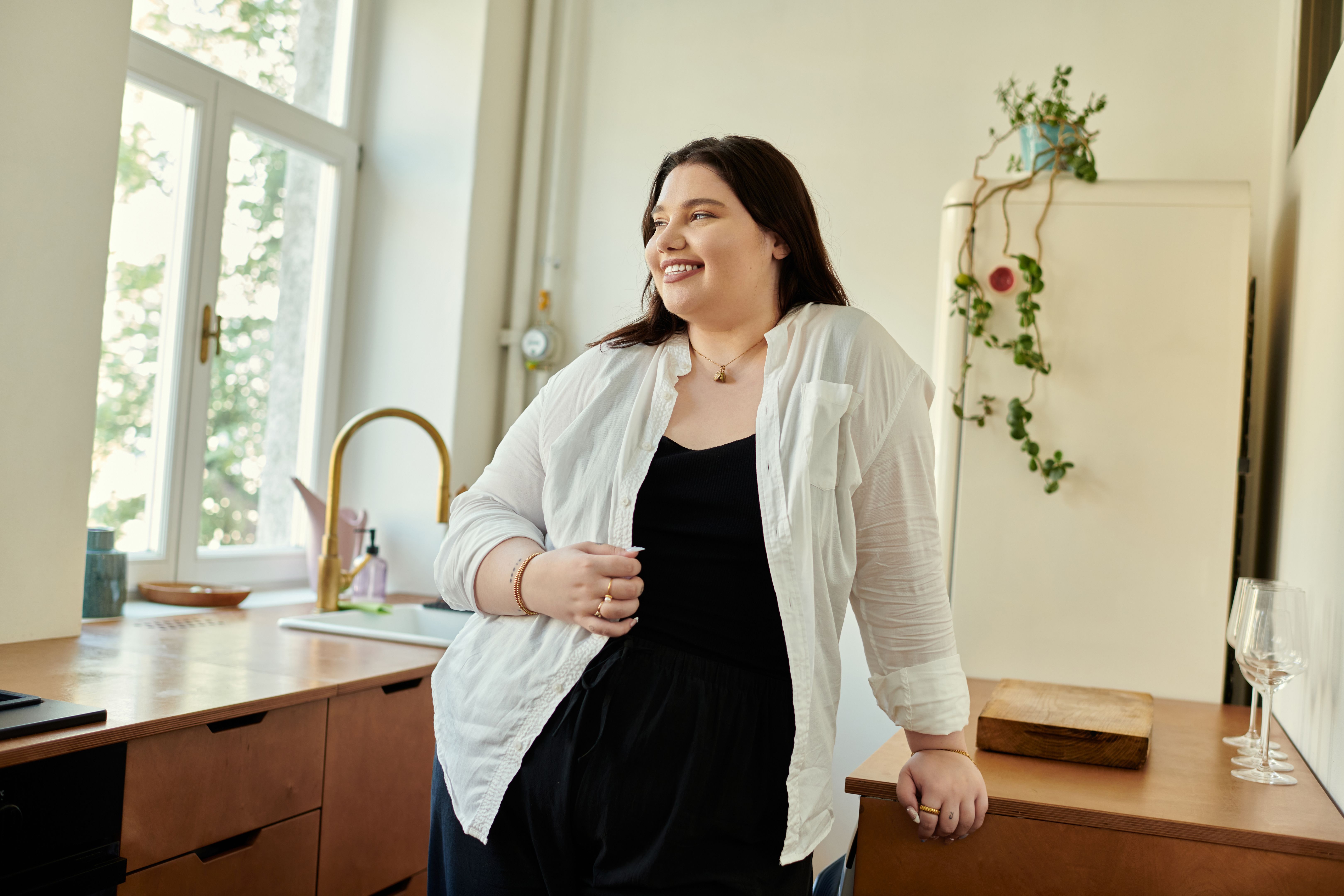 Joyful Plus Size Woman Smiling at Home in Modern Kitchen During Bright Daytime