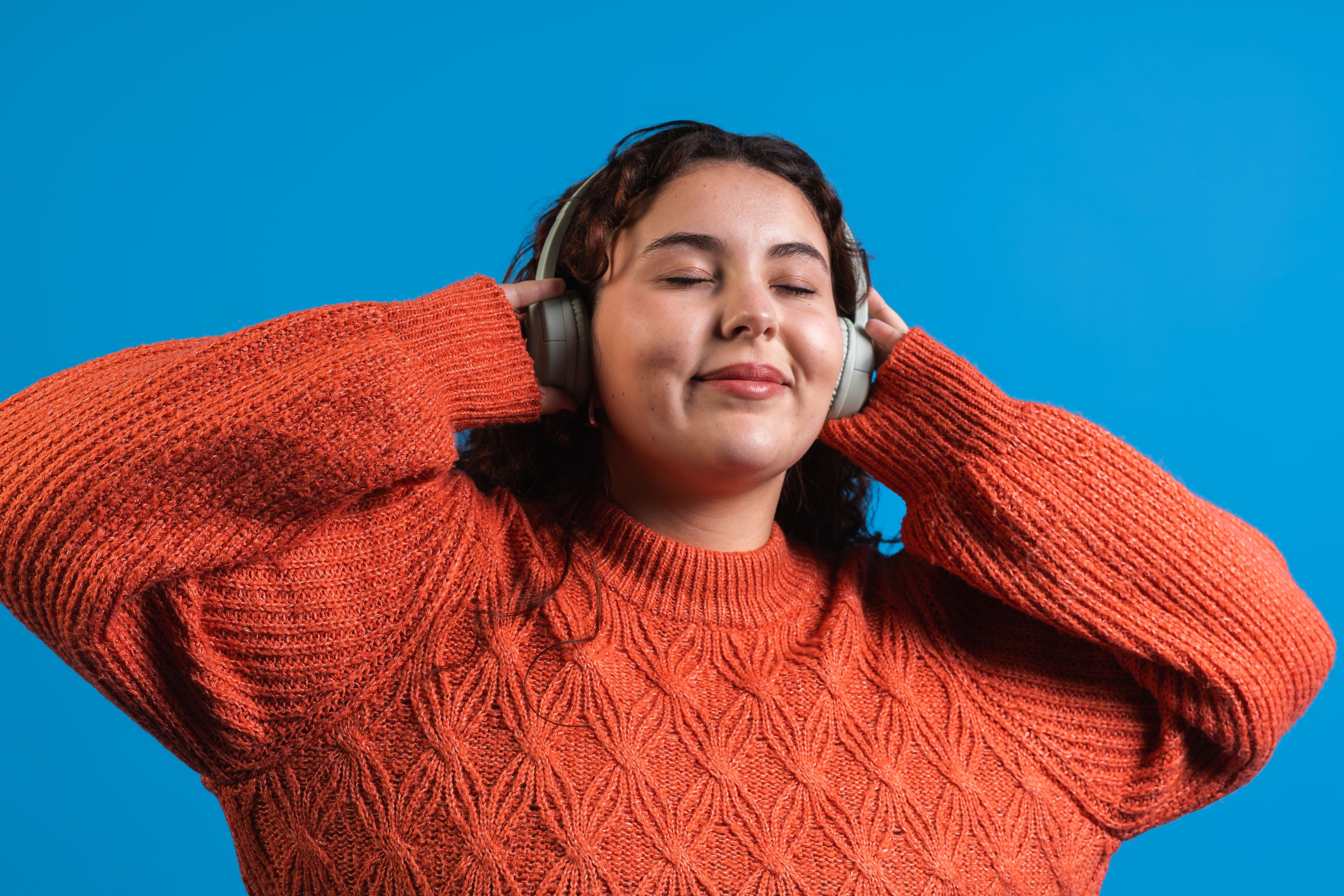Young woman enjoying music with wireless headphones and closing eyes on blue background Young woman enjoying music with wireless headphones and closing eyes on blue background