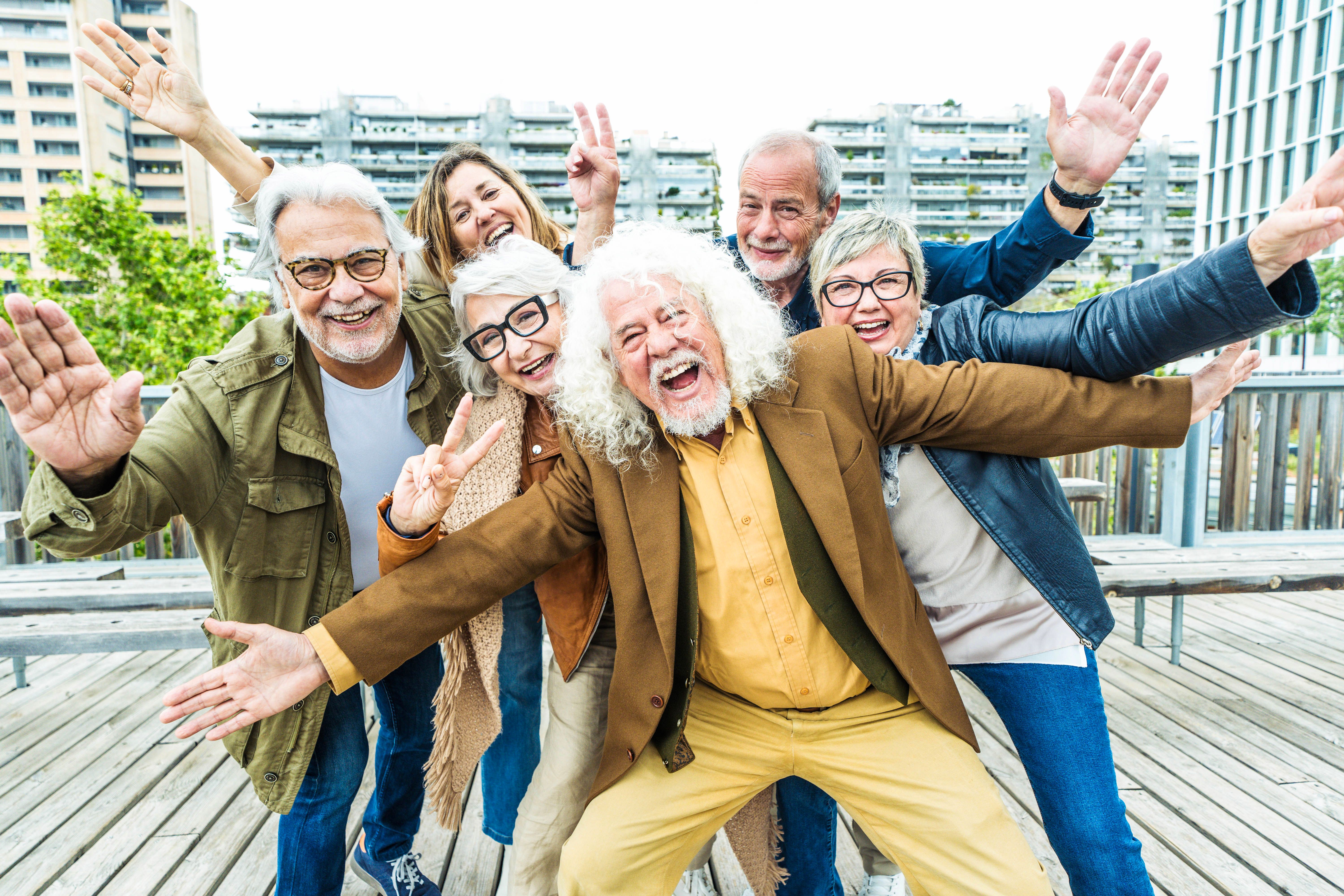 Happy group of senior people smiling together at camera outside - Delightful older friends enjoying day out walking on city street - Aged male and females pensioners hugging together outdoors Happy group of senior people smiling together at camera outside - Delightful older friends enjoying day out walking on city street - Aged male and females pensioners hugging together outdoors