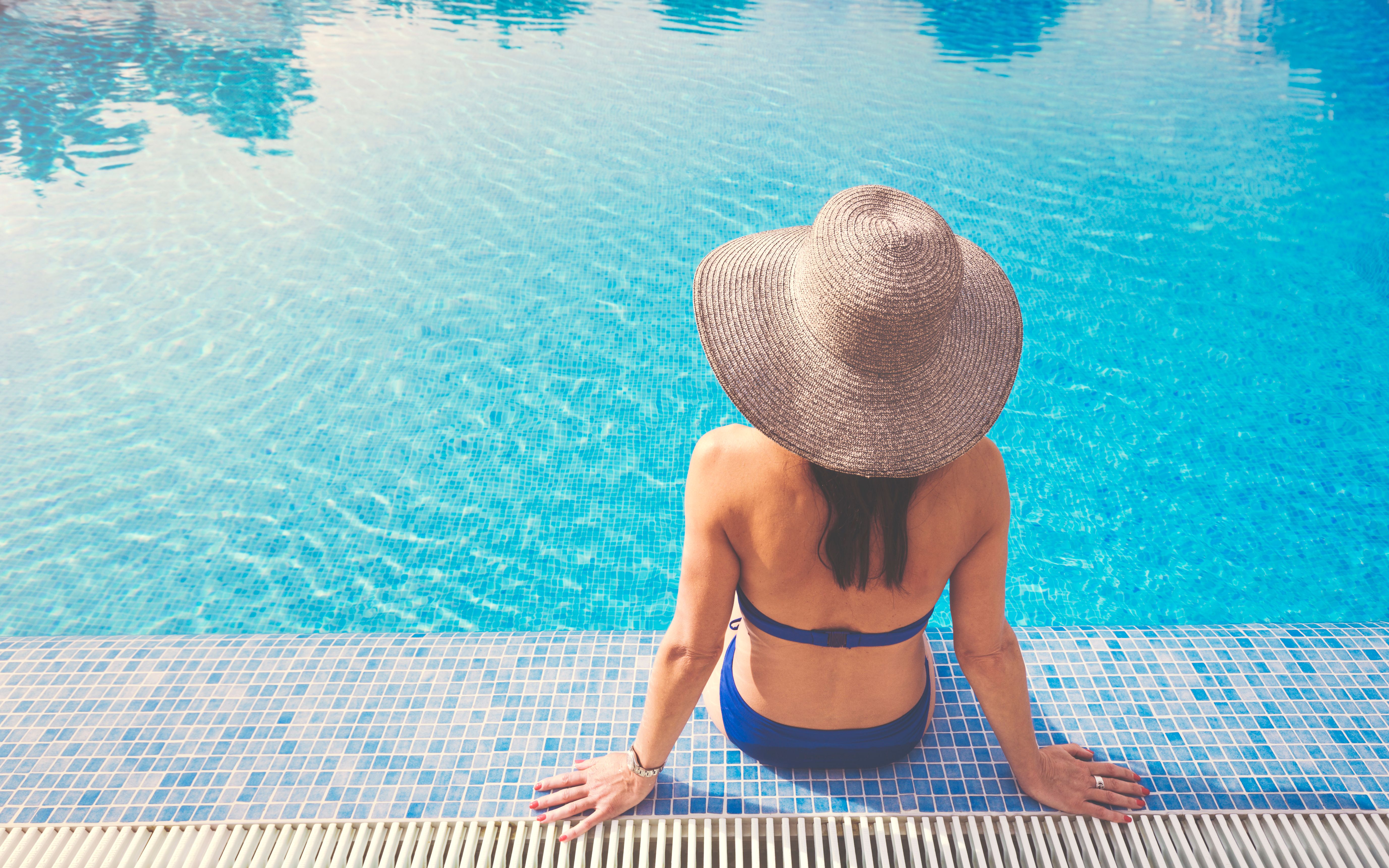Beautiful Woman relaxing in swimming pool with sun hat