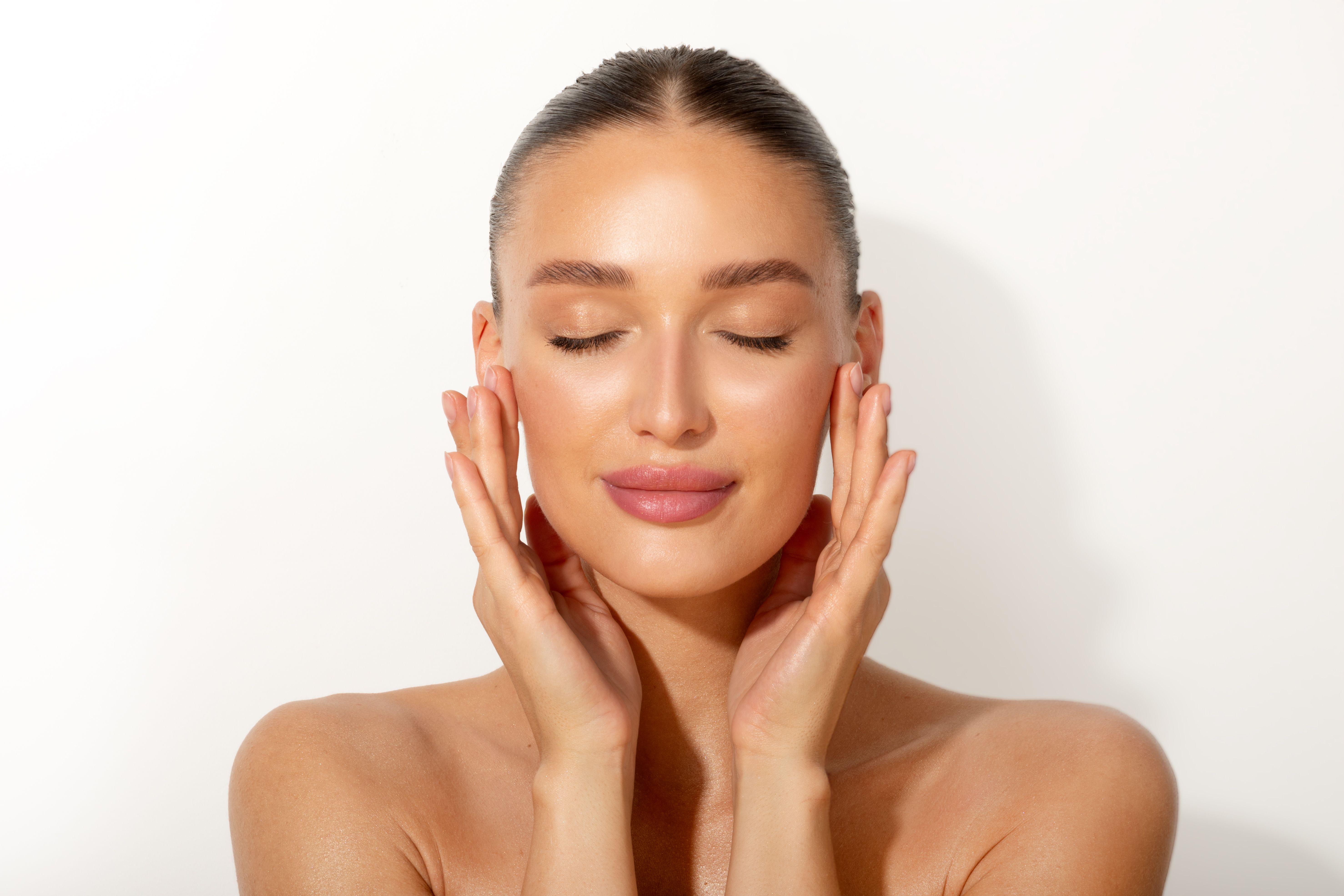 Perfect skin. Beautiful young European woman with nude makeup touching her cheeks with pleased face expression over white background