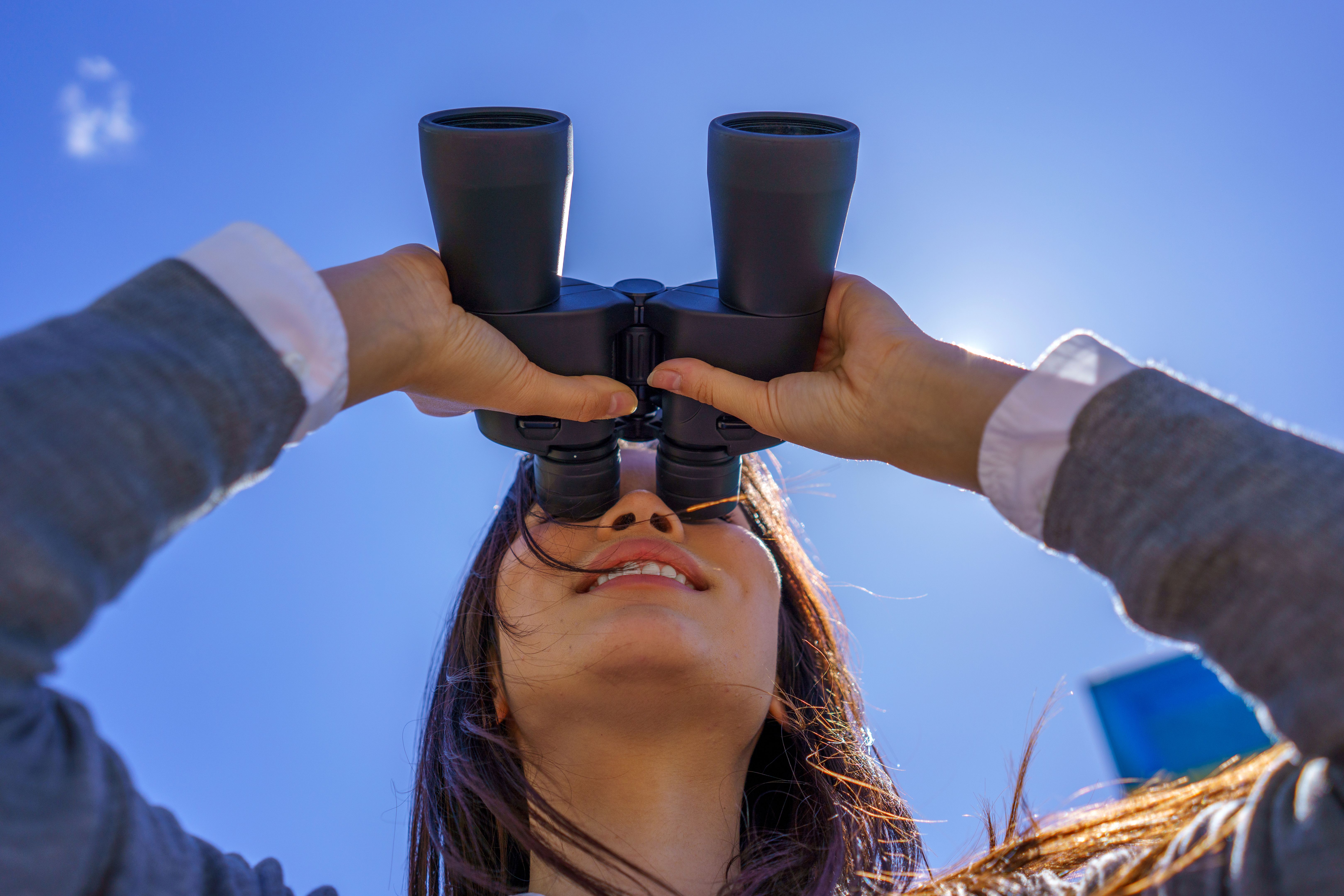 Young Japanese businesswoman looking up with binoculars in the sky
