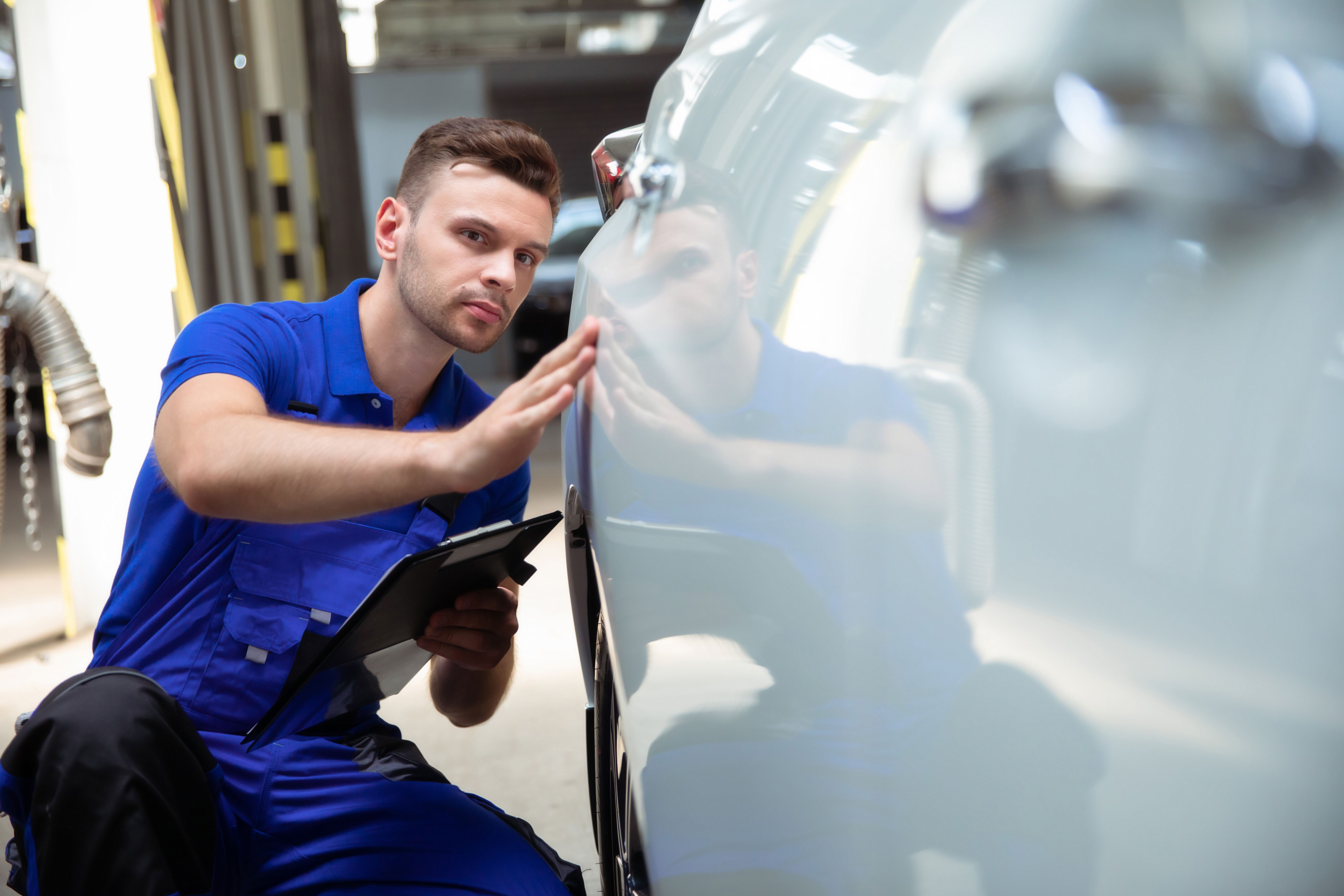 Confident and concentrated young and experienced car auto body repair specialist with a tablet in his hand inspects and diagnosis the car for breakdowns Confident and concentrated young and experienced car auto body repair specialist with a tablet in his hand inspects and diagnosis the car for breakdowns