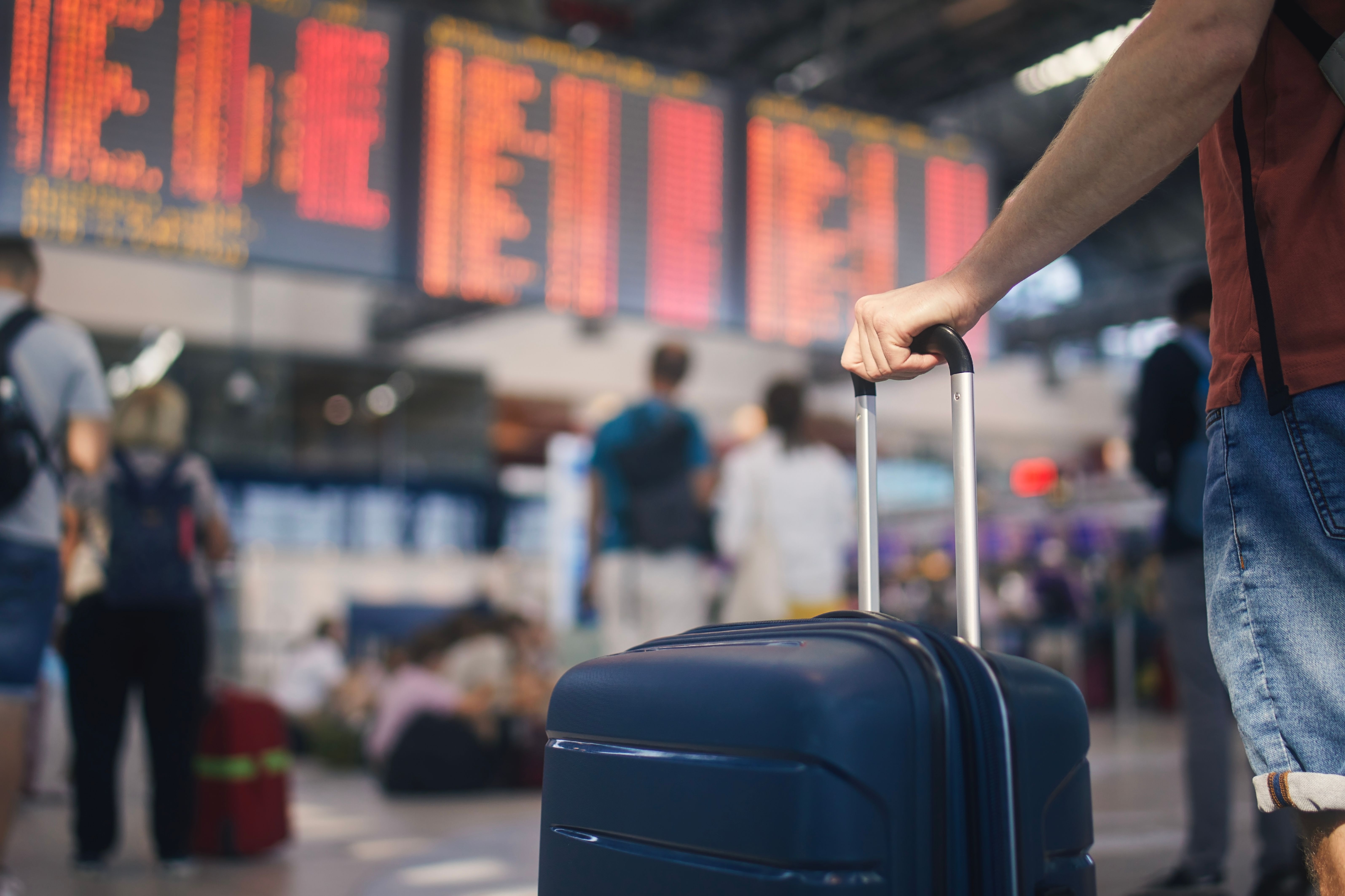 Hand of man while holding suitcase against arrival and departure board at airport Hand of man while holding suitcase against arrival and departure board at airport