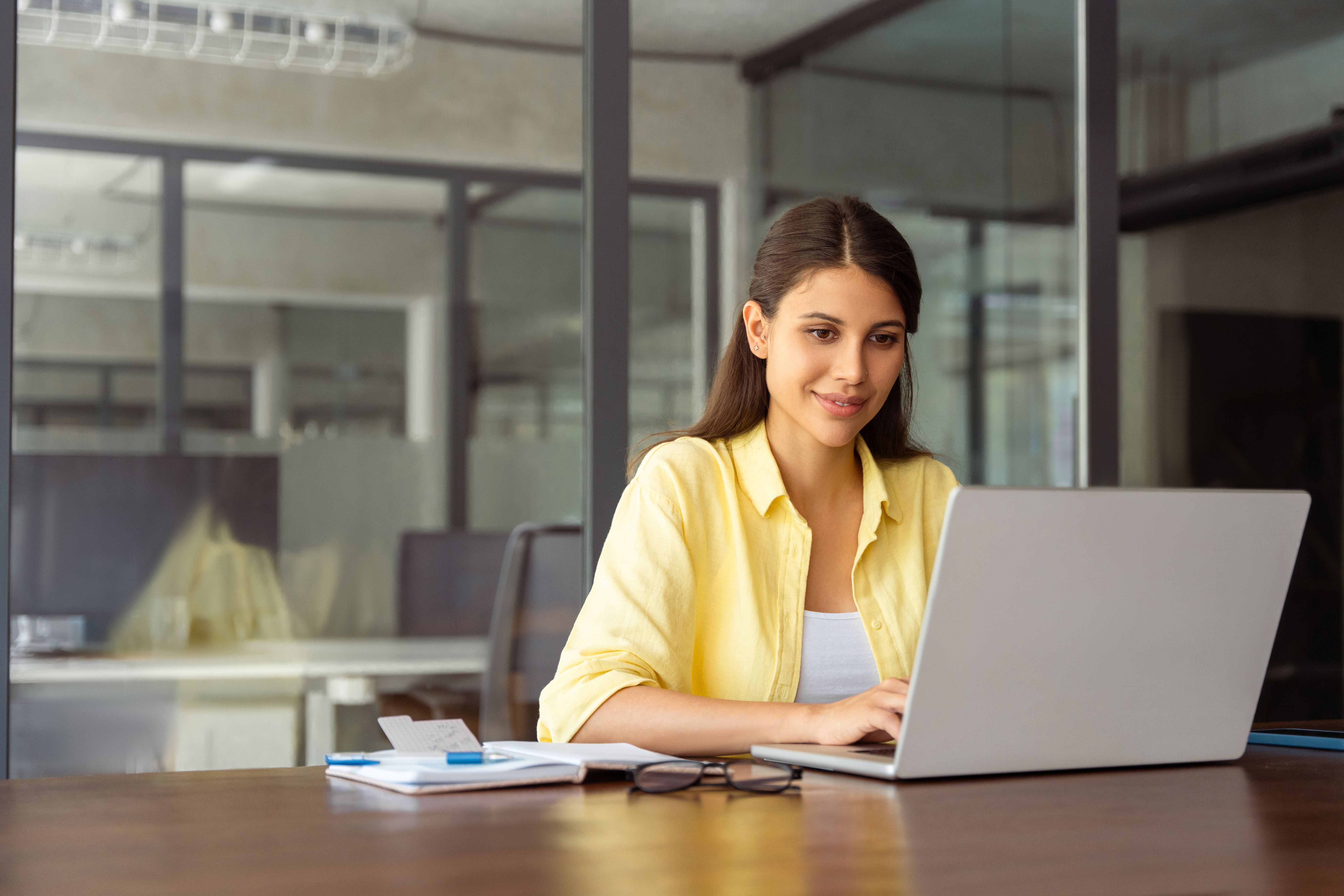 Smiling latin hispanic female marketing manager, professional it specialist working, browsing at laptop computer sitting at desk in modern office. Cheerful young woman employee using pc for business Smiling latin hispanic female marketing manager, professional it specialist working, browsing at laptop computer sitting at desk in modern office. Cheerful young woman employee using pc for business