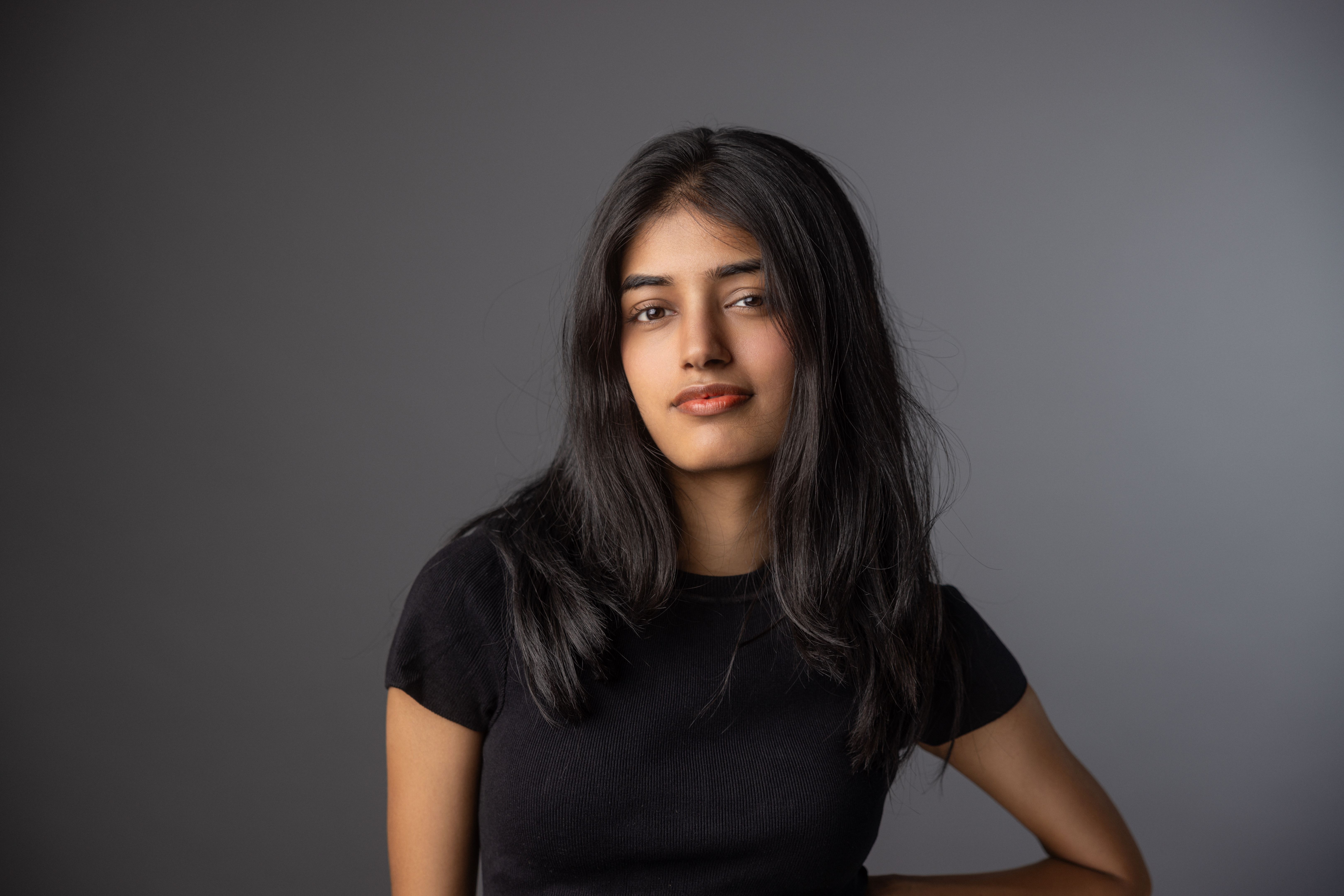 Young Indian girl smiling standing in front of a grey background