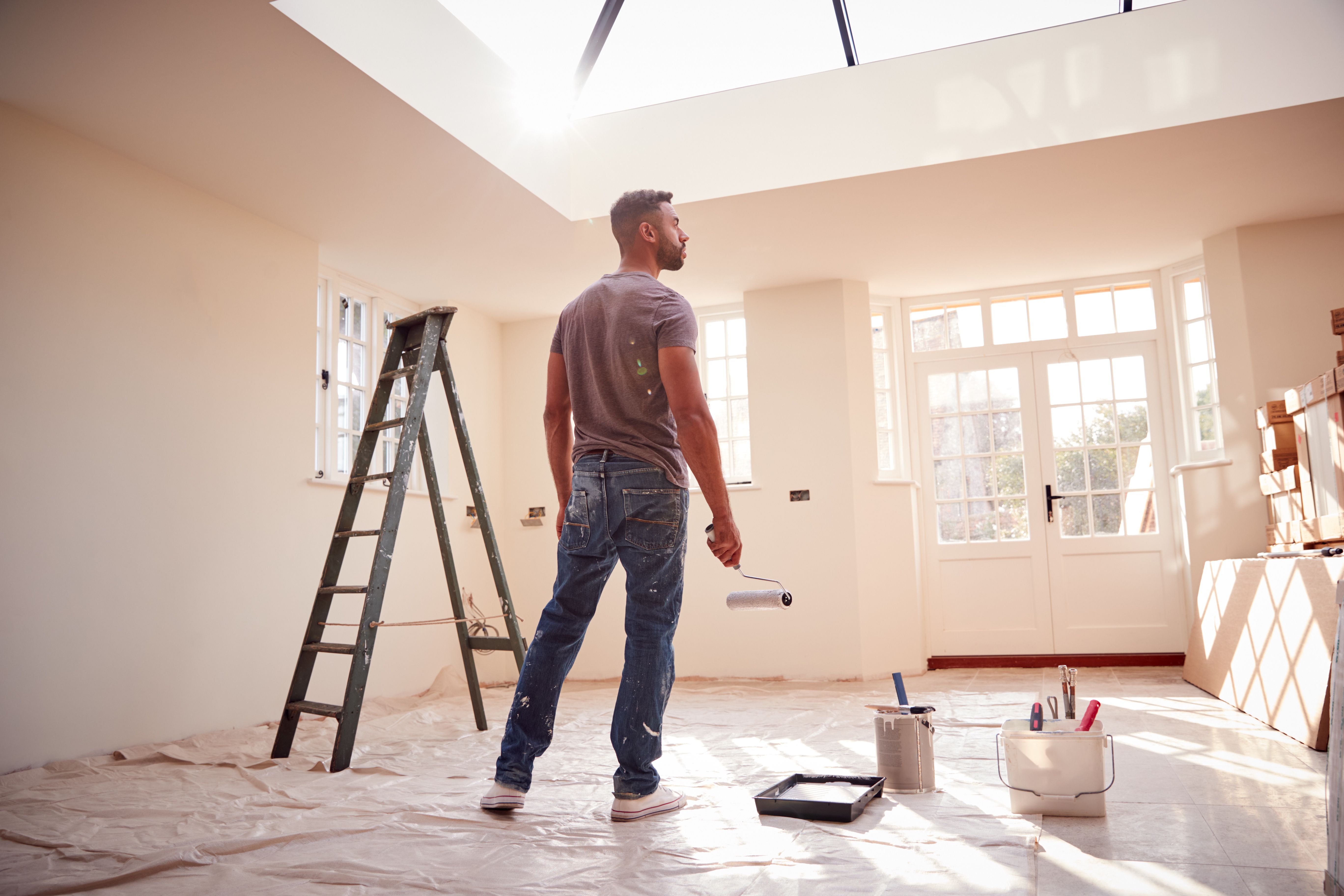 Rear View Of Man Holding Paint Roller Decorating New Home
