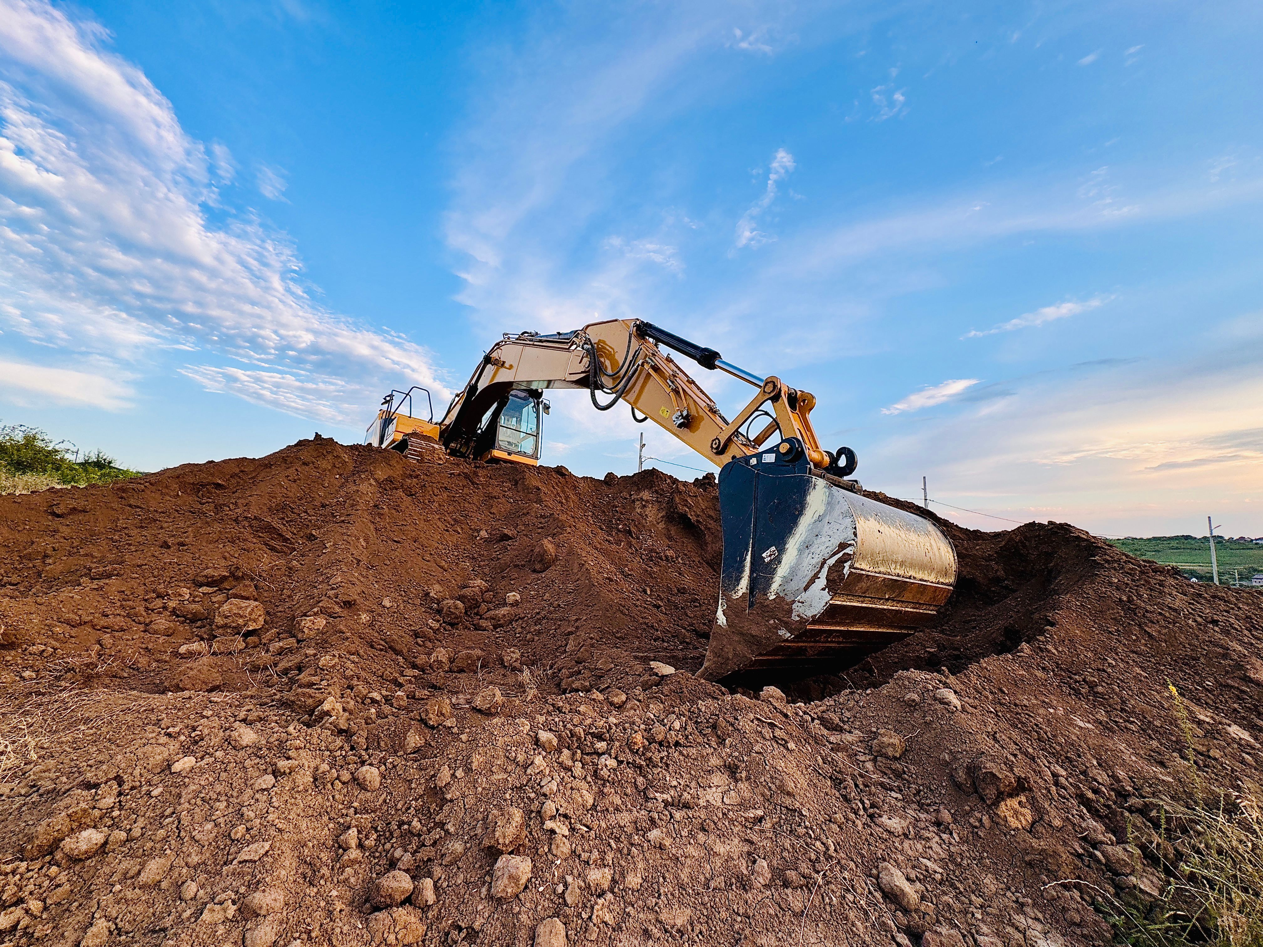 Excavator on Dirt Hill with Cloudy Sky