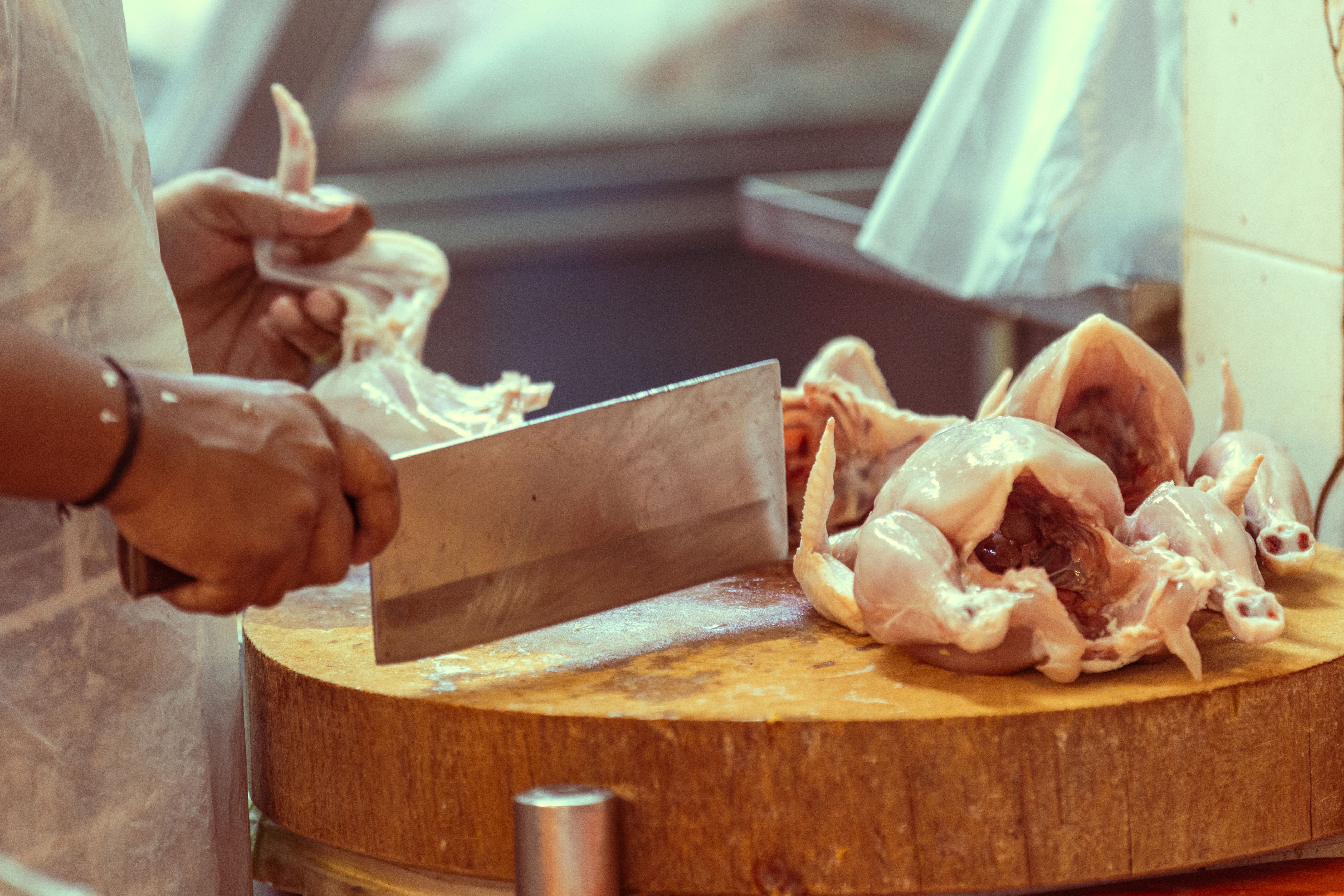Indian butcher is cutting chicken on wood.