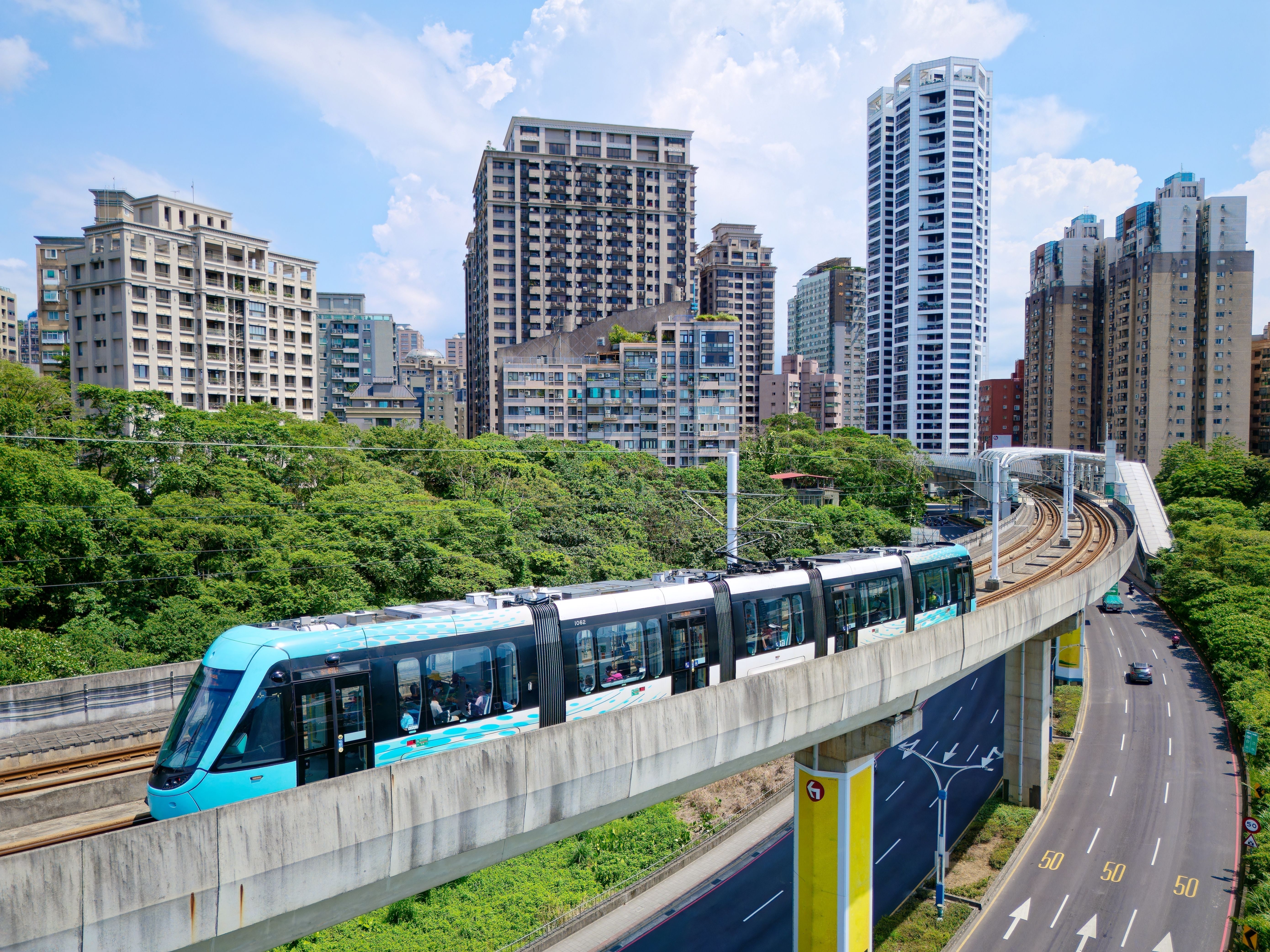 A metro tram dashing on the elevated track of Danhai Light Rail Transit near Ganzhenlin Station, with booming residential towers in the nearby community, in Tamsui District, New Taipei City, Taiwan