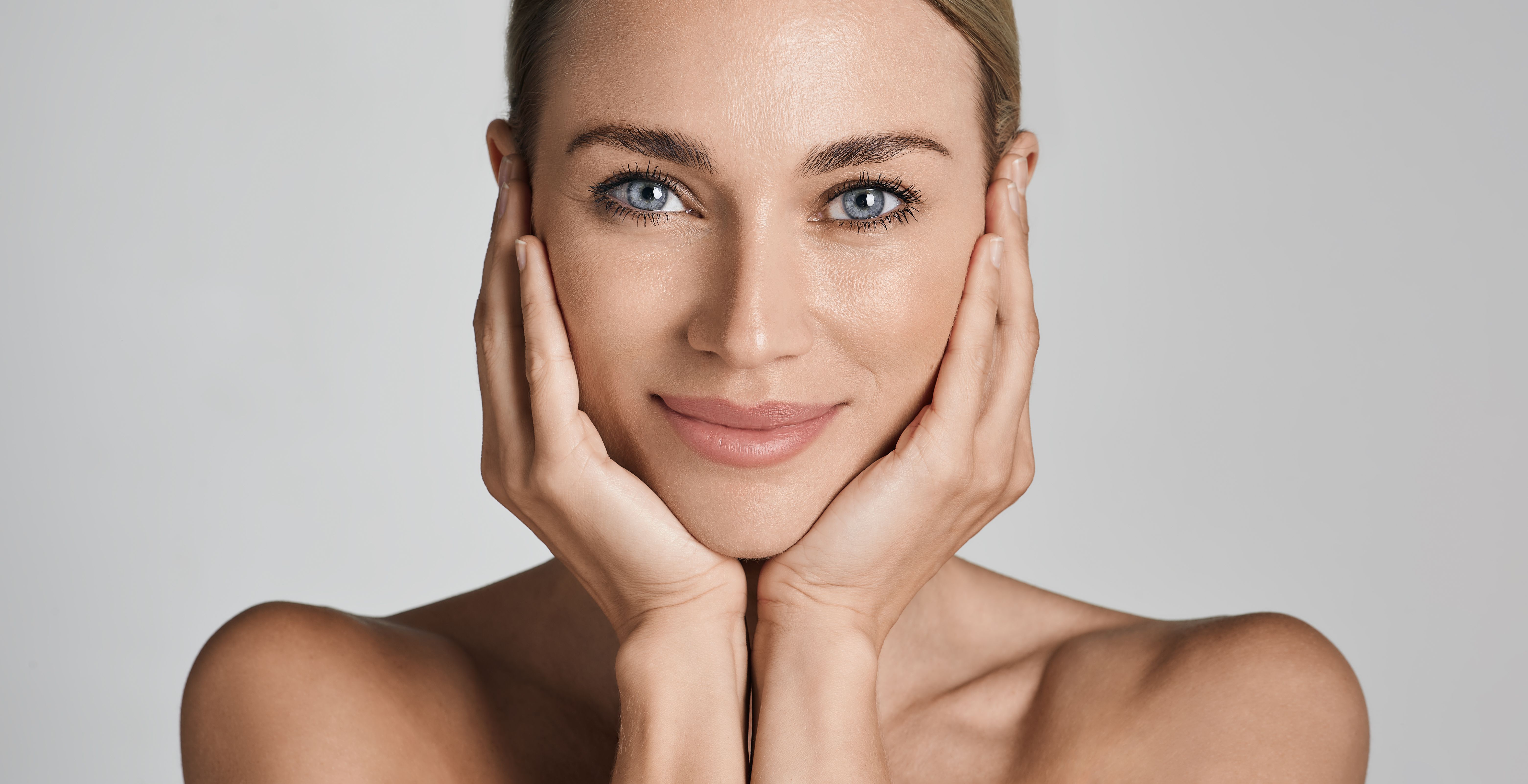 Skin care. Beautiful woman with healthy facial skin touching hands moisturized face skin, on light grey background. High quality Skin care. Beautiful woman with healthy facial skin touching hands moisturized face skin, on light grey background. High quality