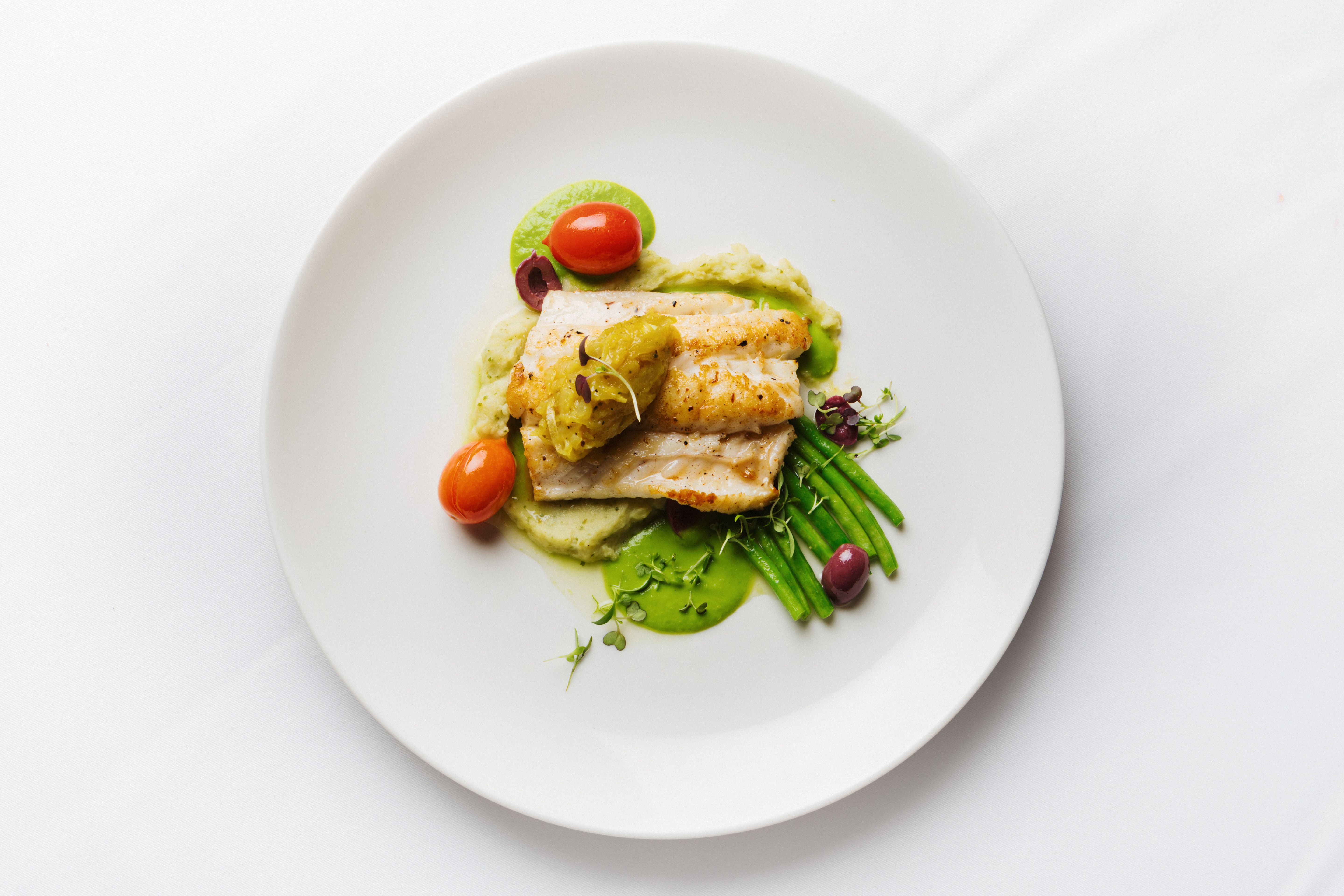 Grilled fish served in a fine restaurant with green beans, mash, cherry tomatoes, olives and microgreens