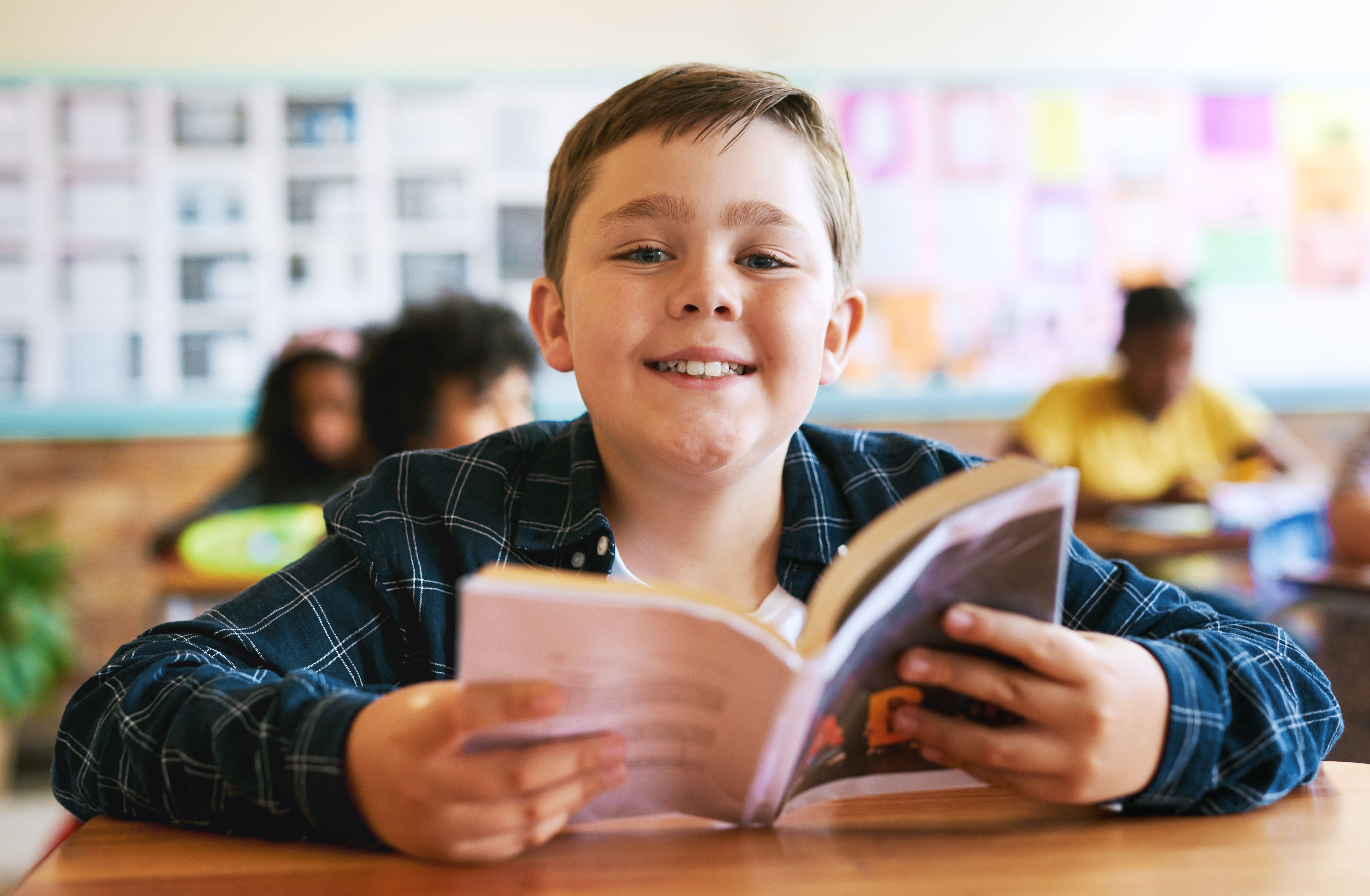 Shot of a young boy sitting in his classroom at school and reading a book