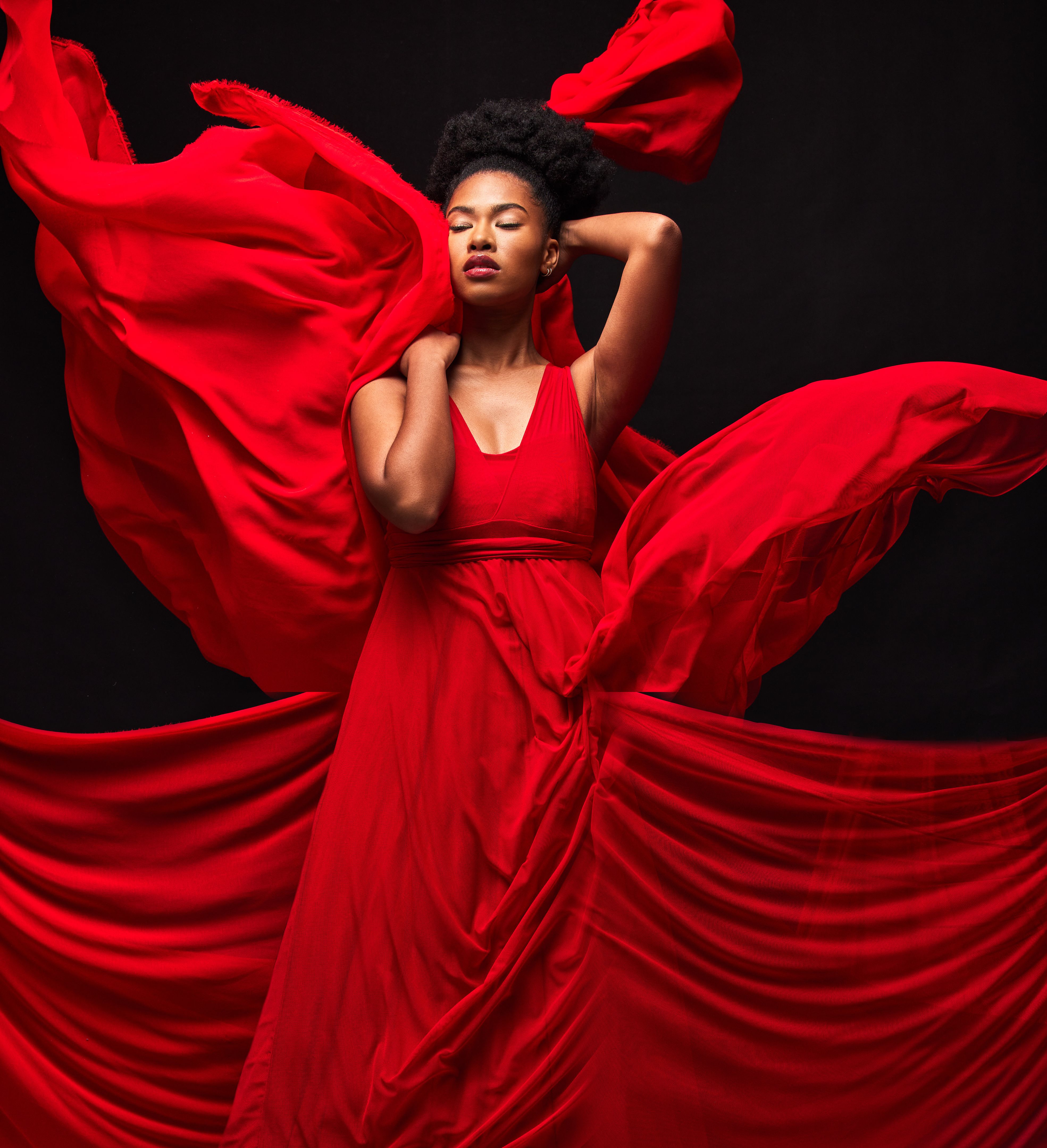 Black woman, art and fashion, red fabric on dark background with motion and aesthetic movement. Flowing silk, fantasy and artistic beauty, stylish African model in creative designer dress in studio.