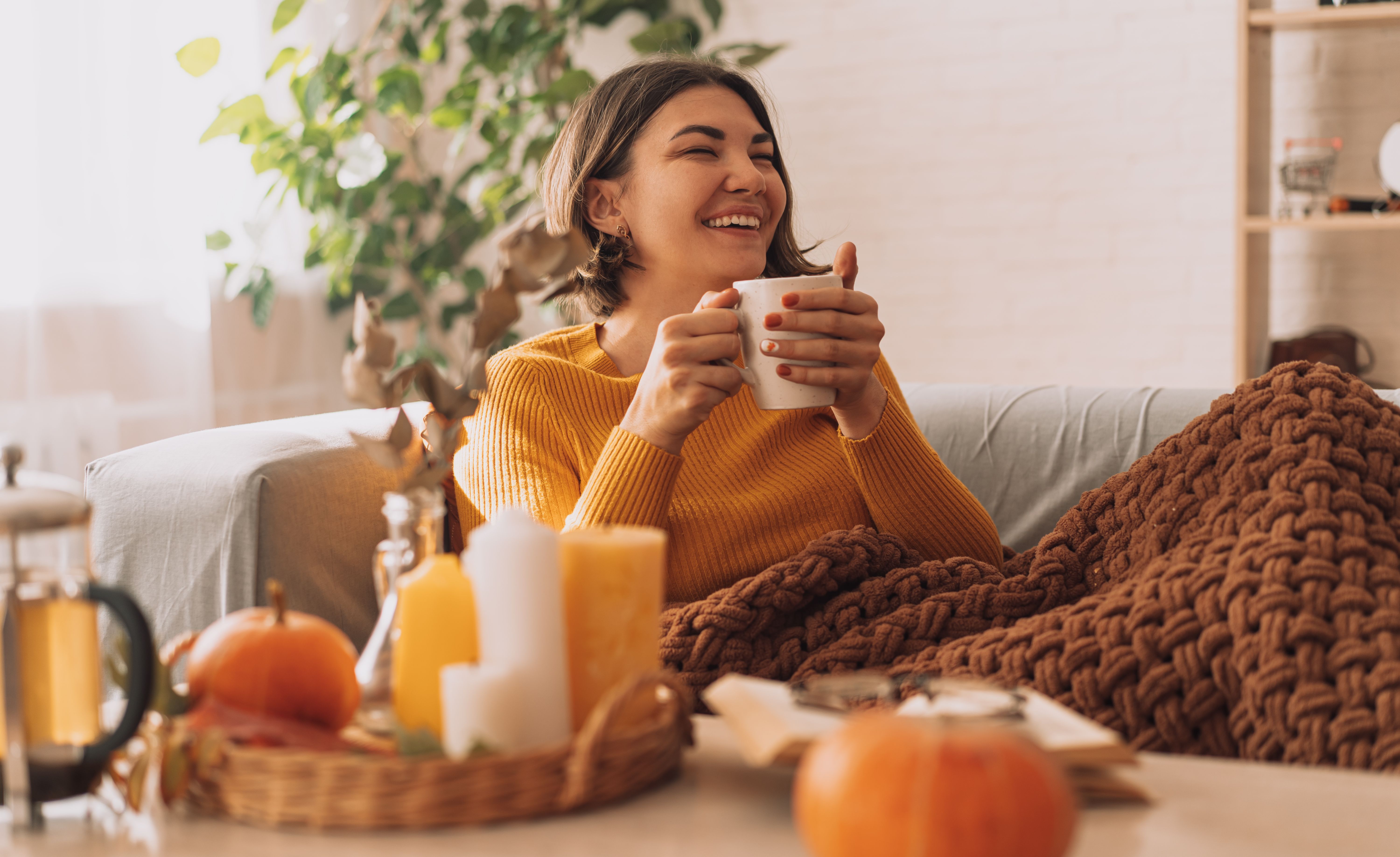 Lady drinks herbal tea brewed in a teapot in front of burning candles and a pumpkin