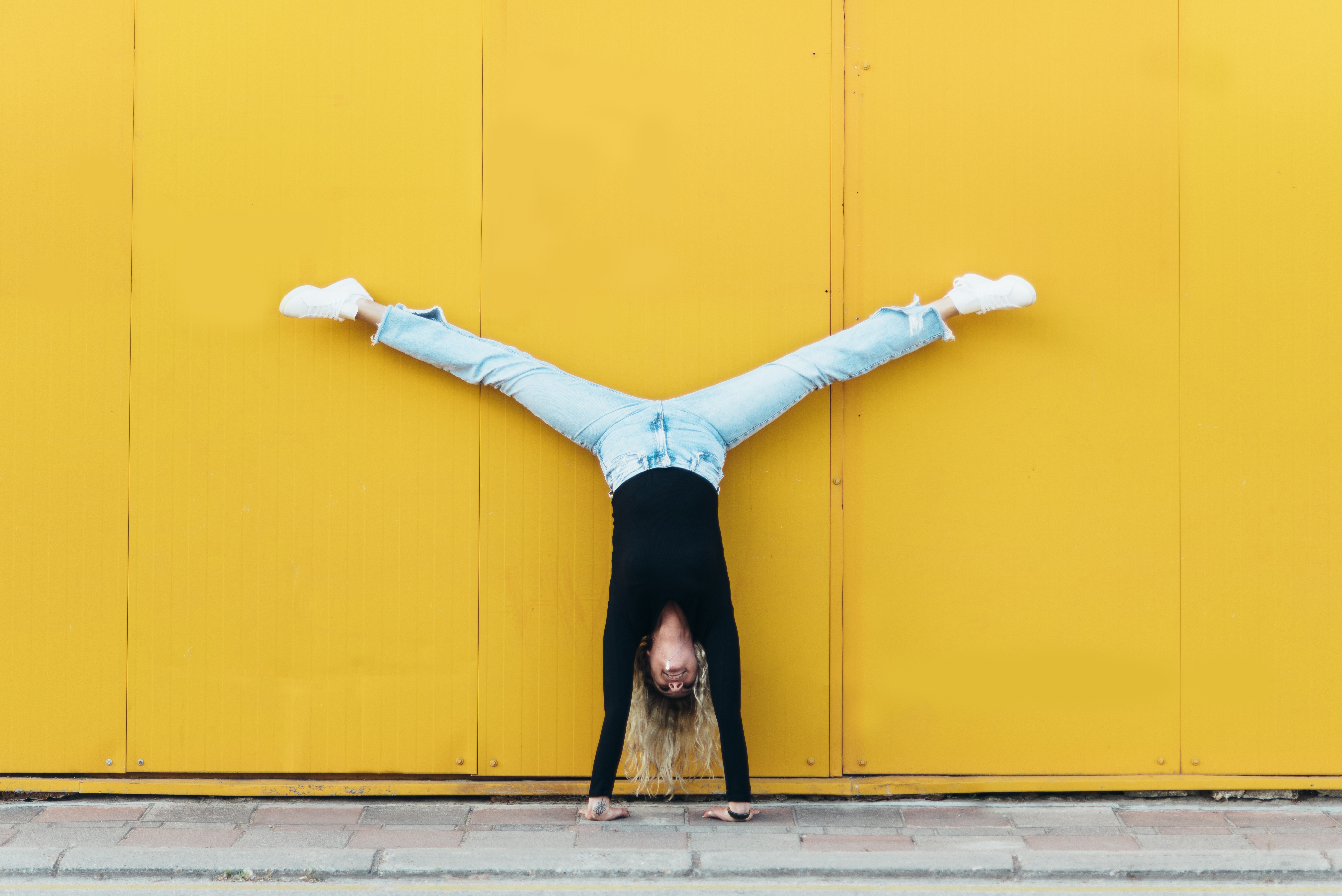 Woman doing hand stand while in front of the yellow wall
