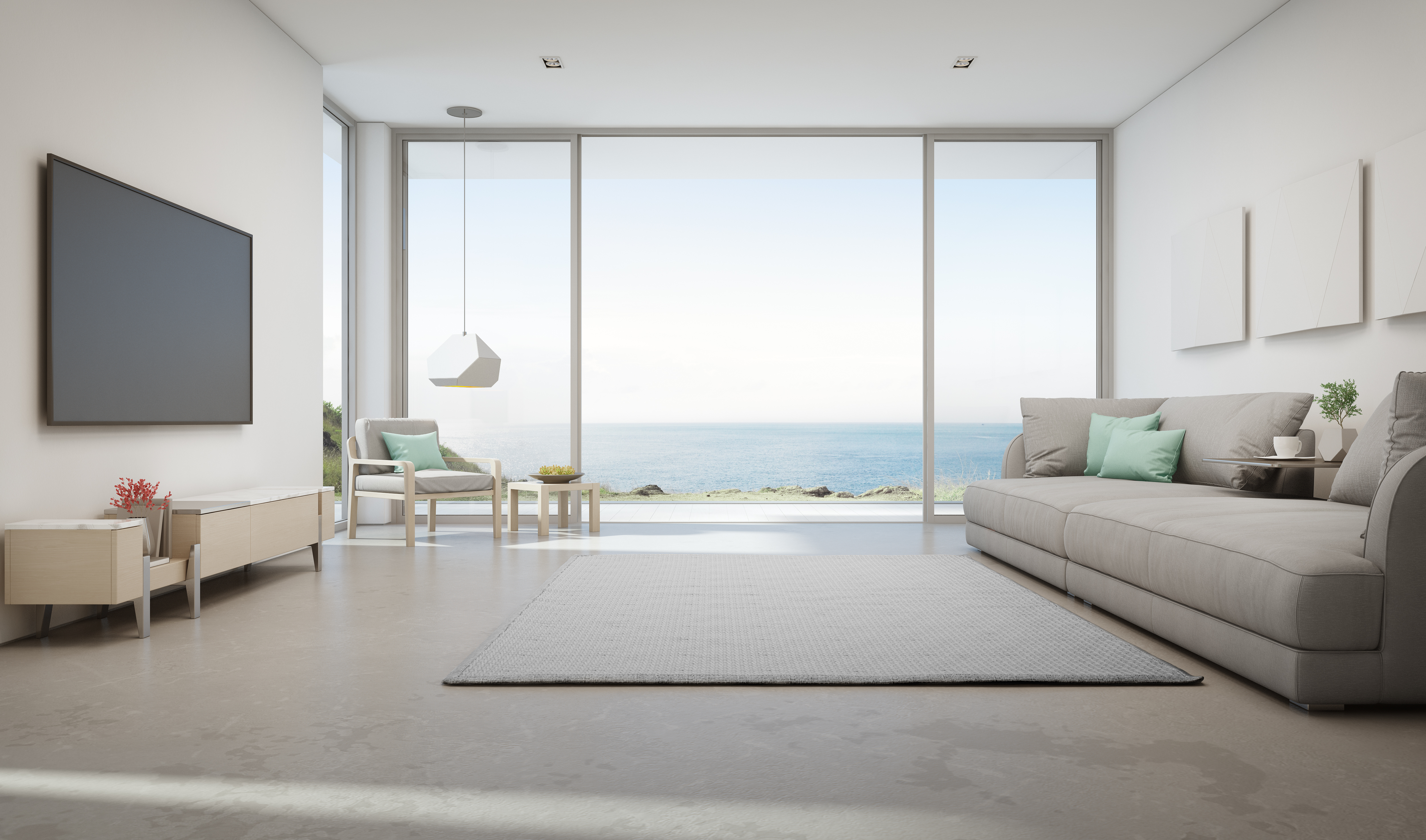 Sea view living room of luxury summer beach house with large glass door and wooden terrace. TV on white wall against big gray sofa in vacation home or holiday villa.