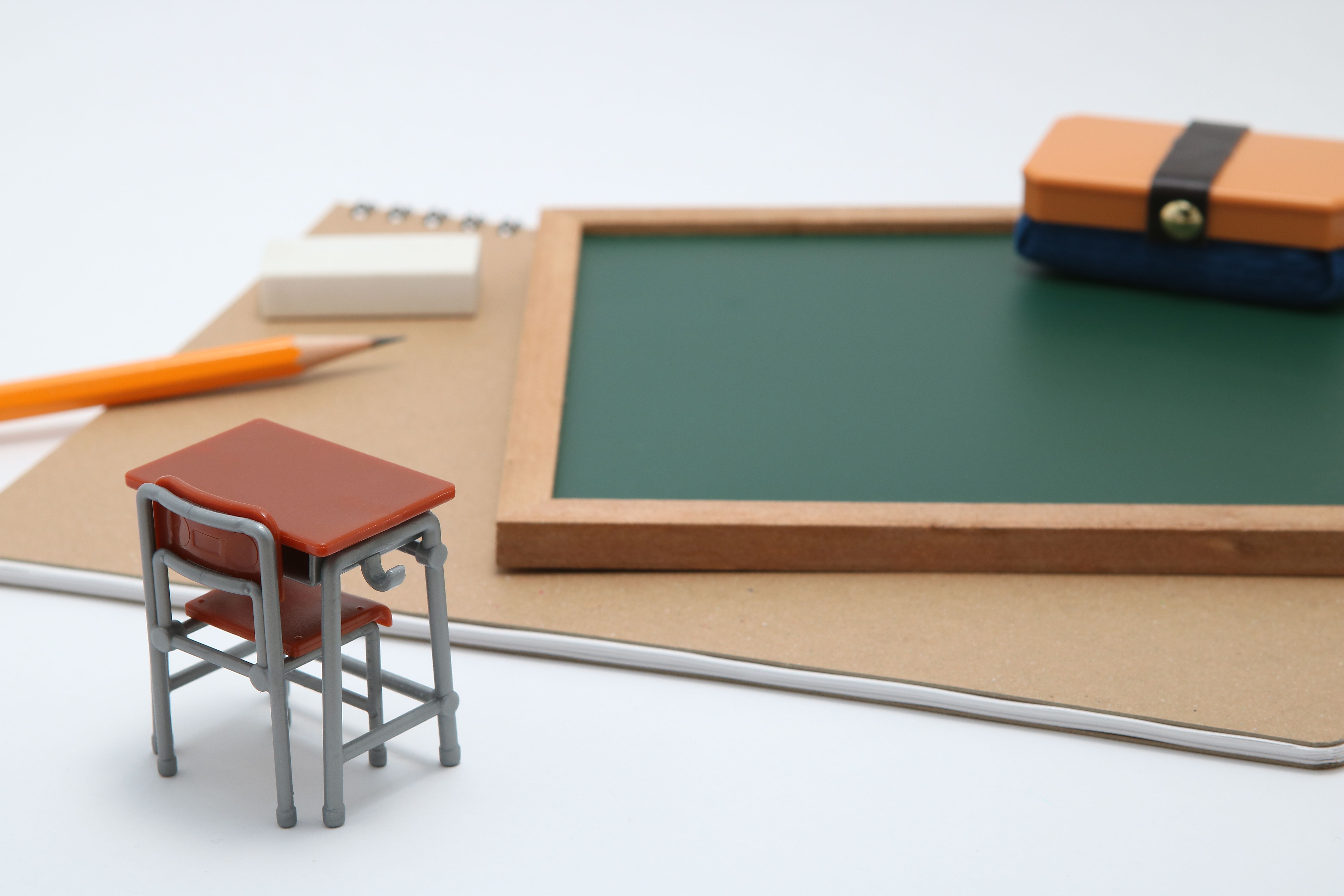Close-Up Of Small Desk By Book And Chalkboard Over White Background